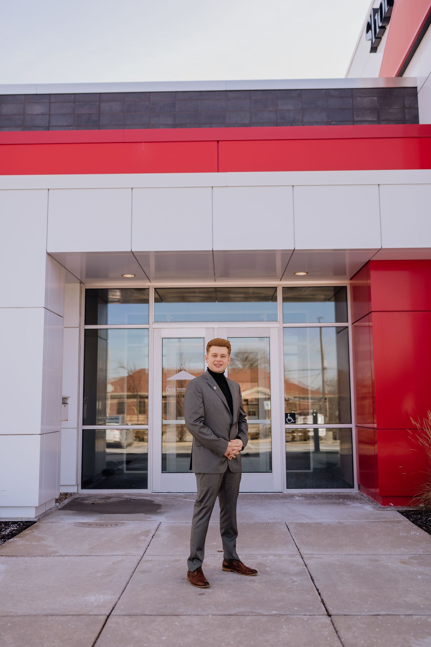 Modern business portrait outside commercial building entrance with red and white architectural details.