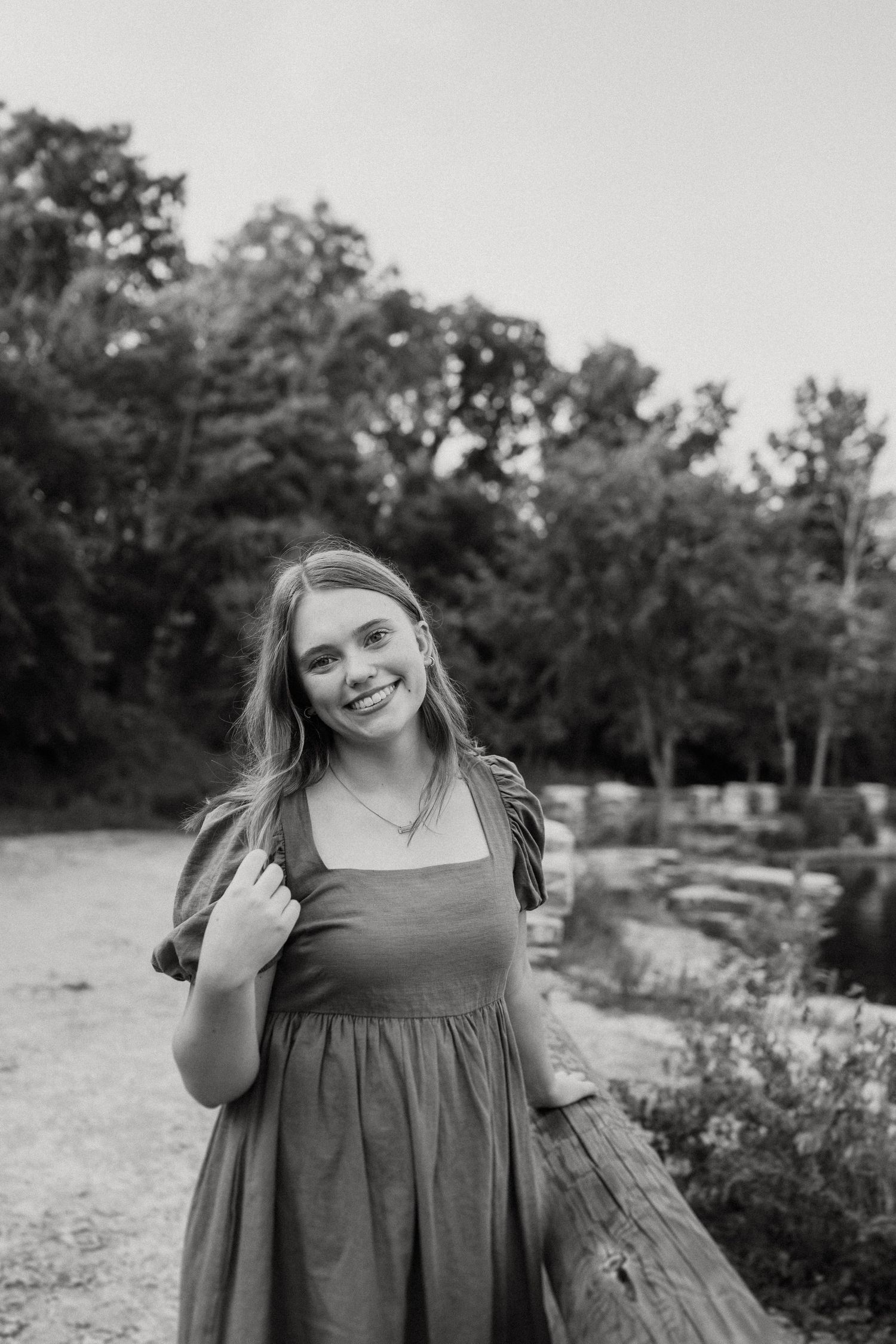 Black and white portrait showing someone in a casual dress by a lakeside path.