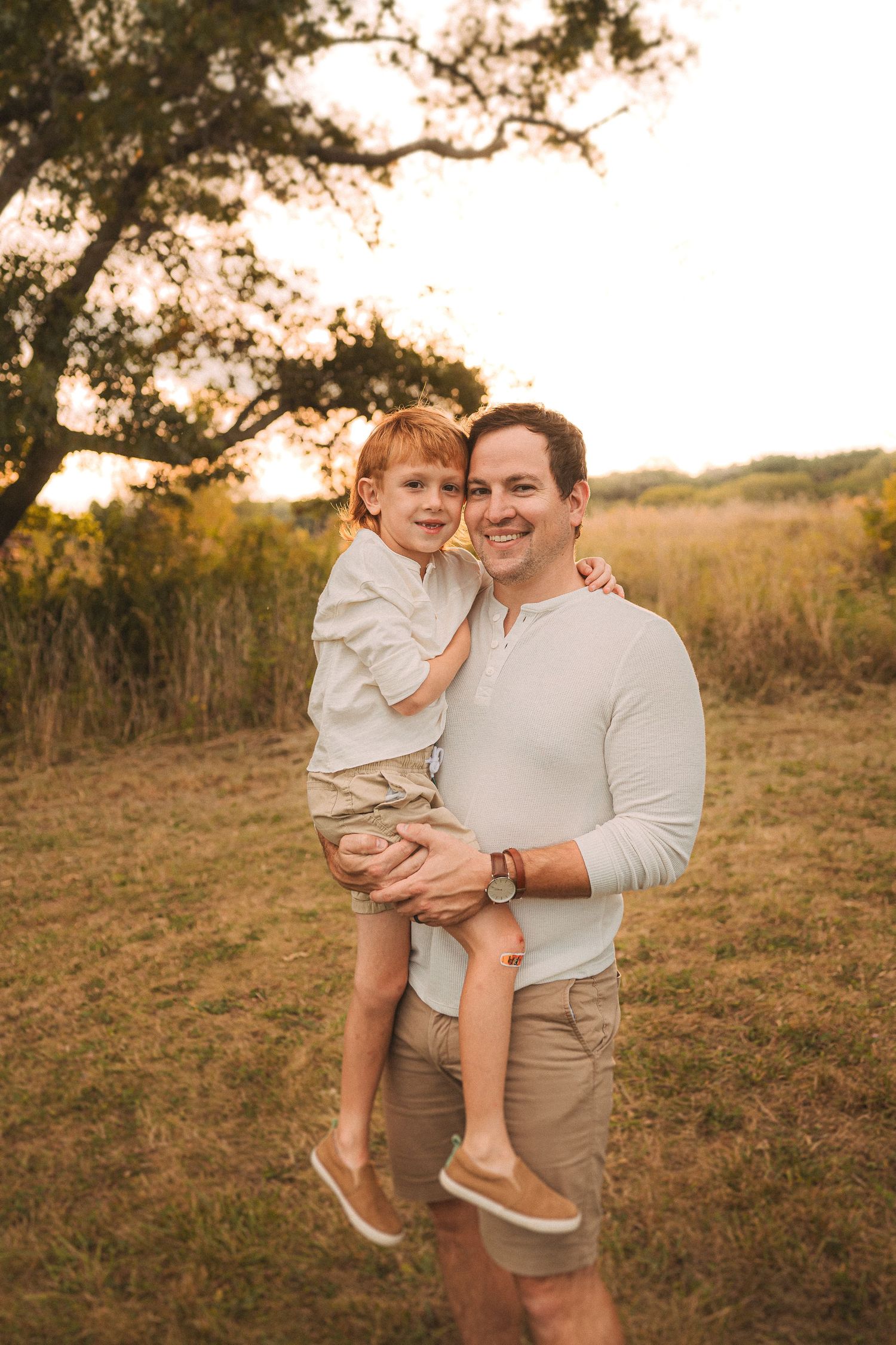 Golden hour portrait of two people embracing under a tree in a field.