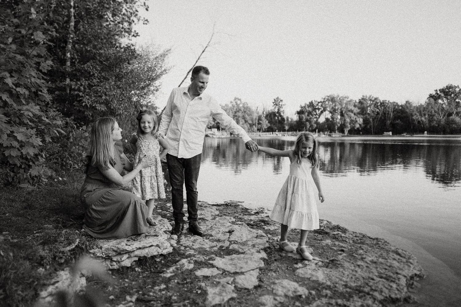 Black and white family portrait by lake showing playful interaction outdoors.