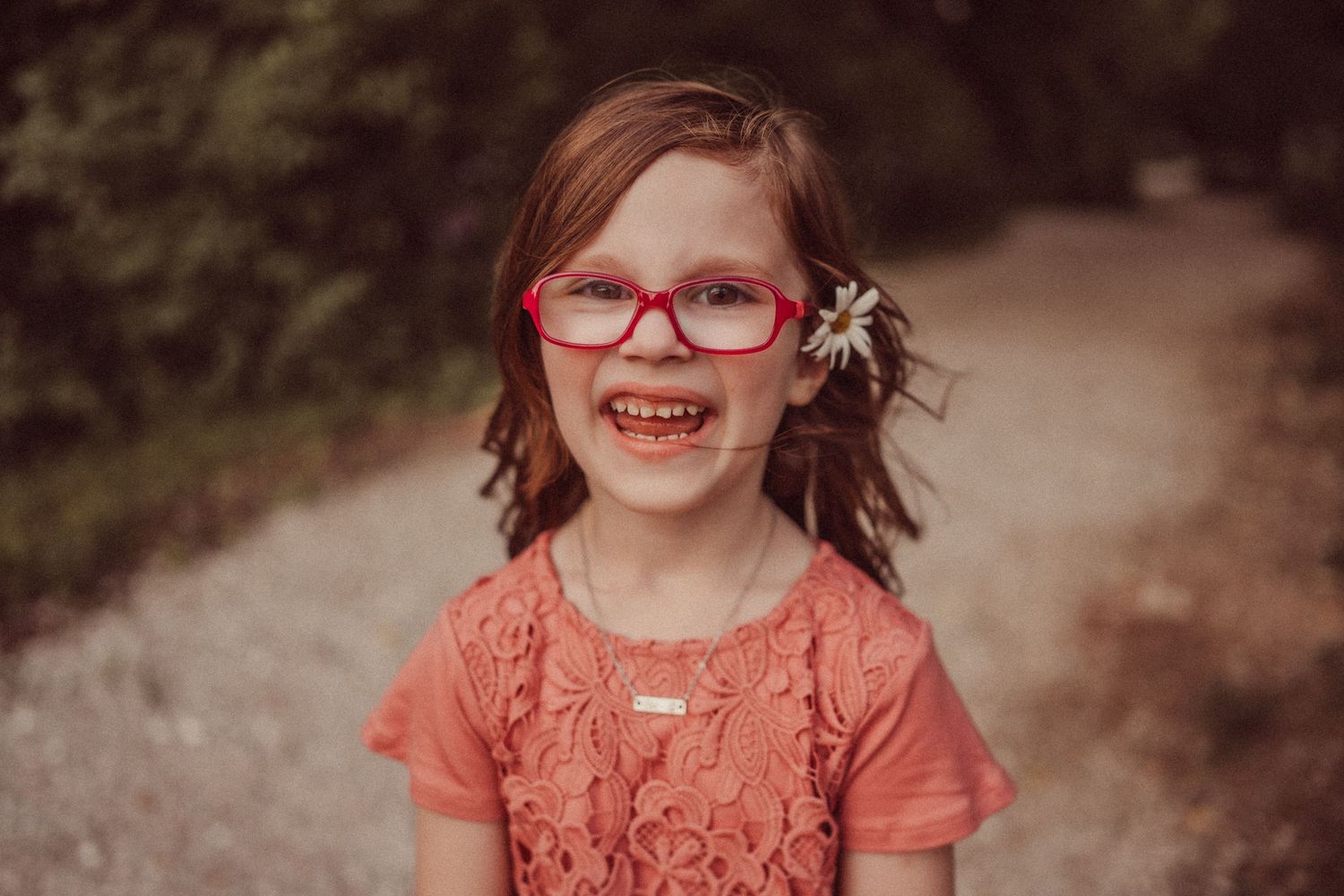 A candid portrait of someone wearing red glasses and a coral top with a joyful expression.