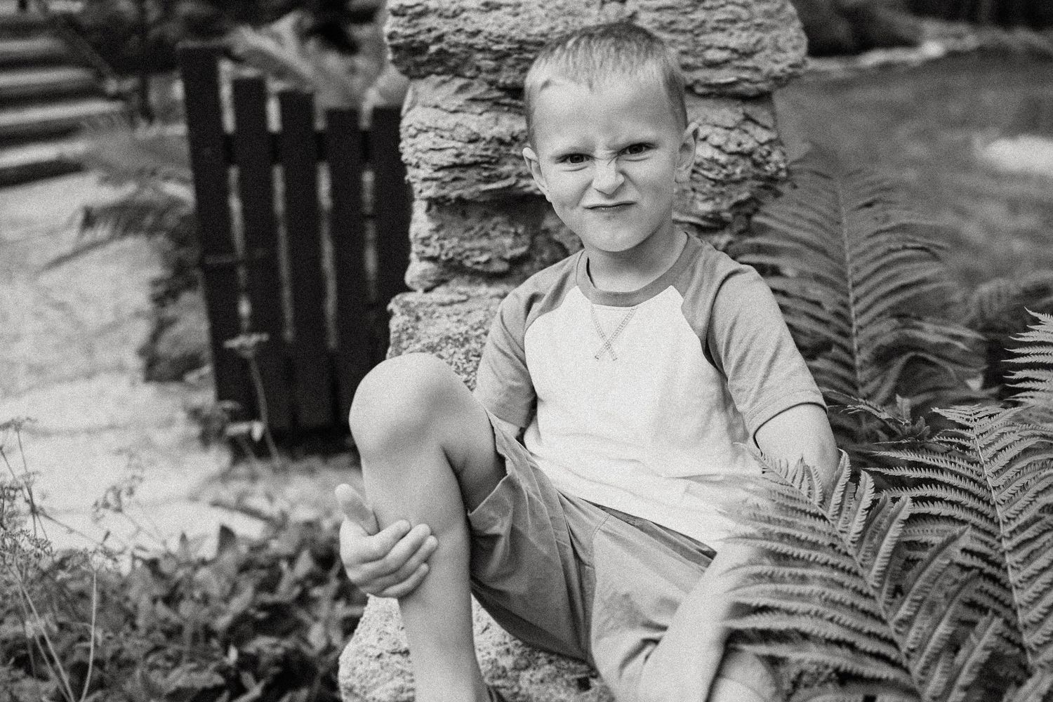 Black and white photo showing casual pose on stone wall with cottage background.
