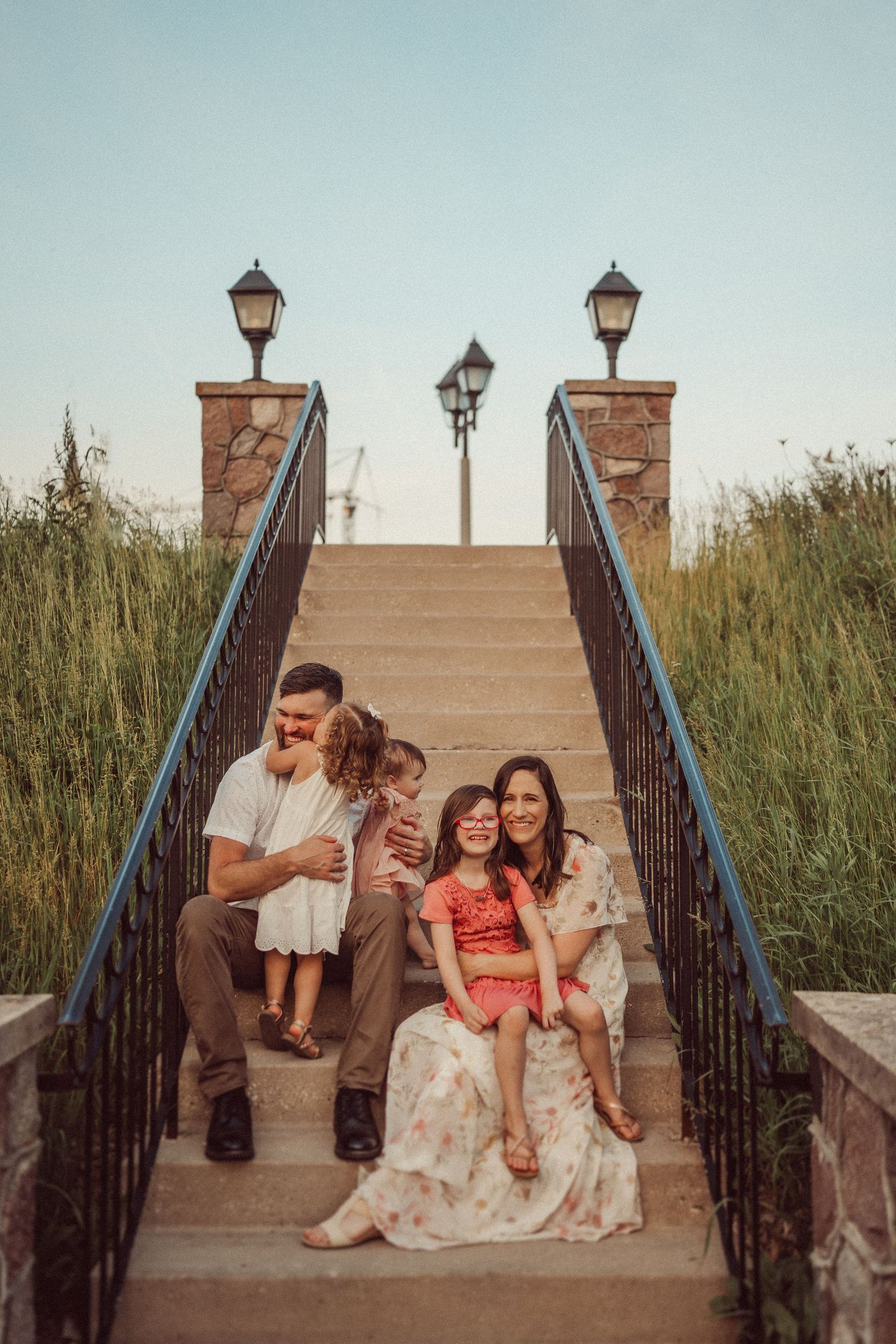 A joyful family portrait on elegant stone steps surrounded by tall grass and vintage lampposts.