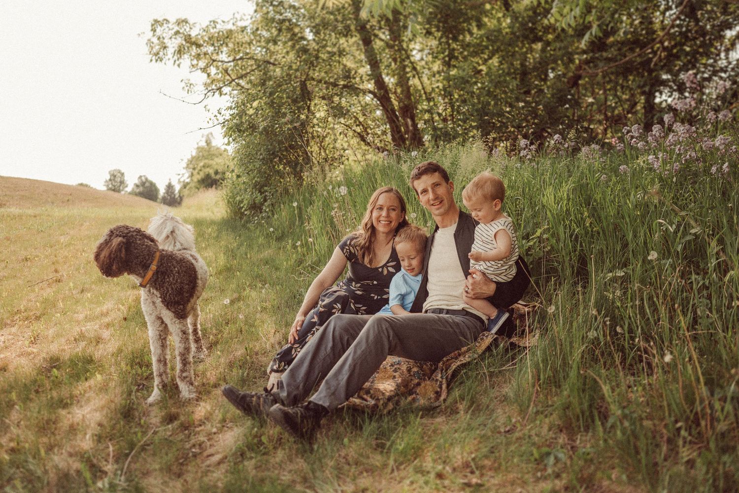 Family sitting outdoors in grassy field with horses on a sunny afternoon.