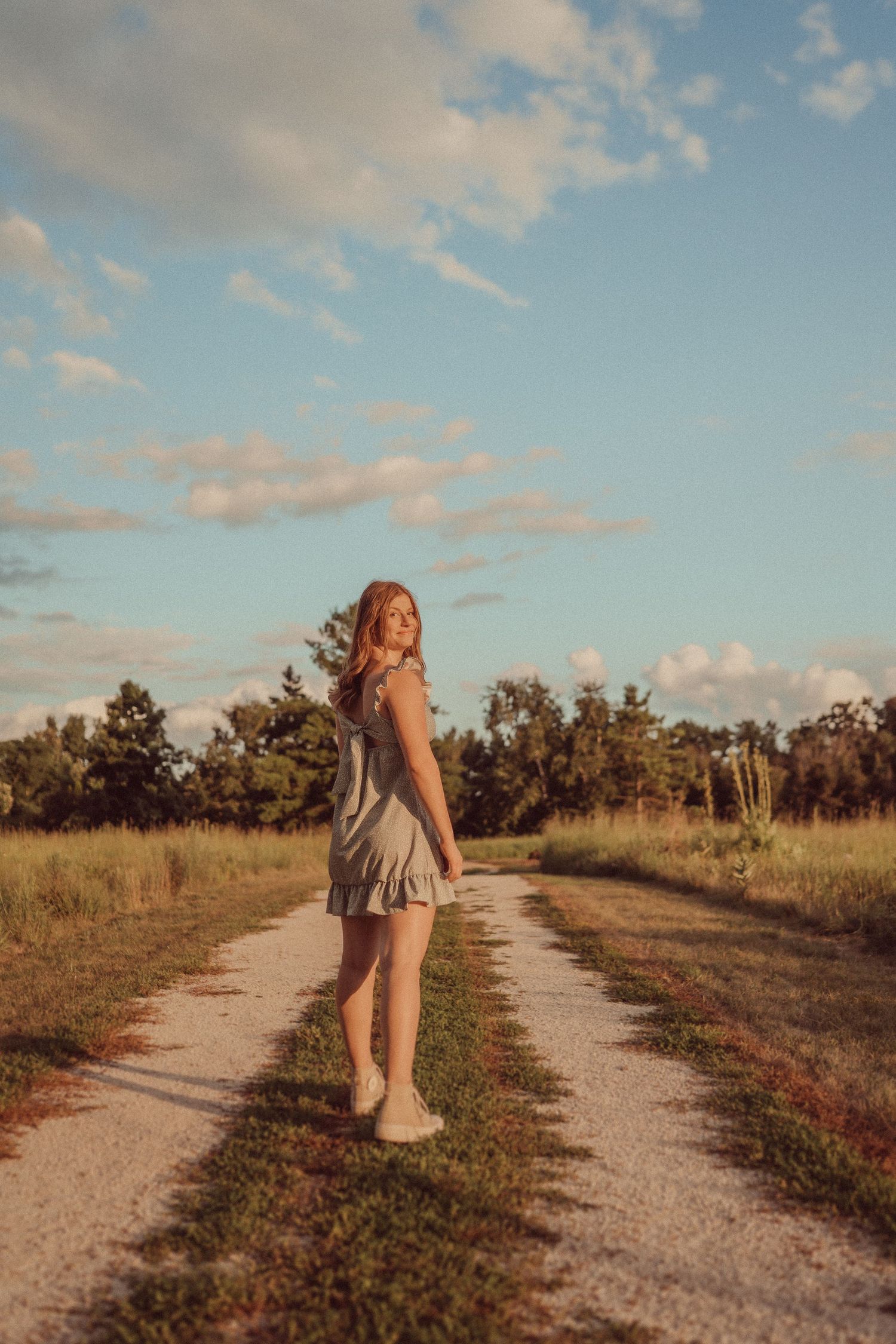 Summery portrait on a winding dirt path with fluffy clouds at golden hour.