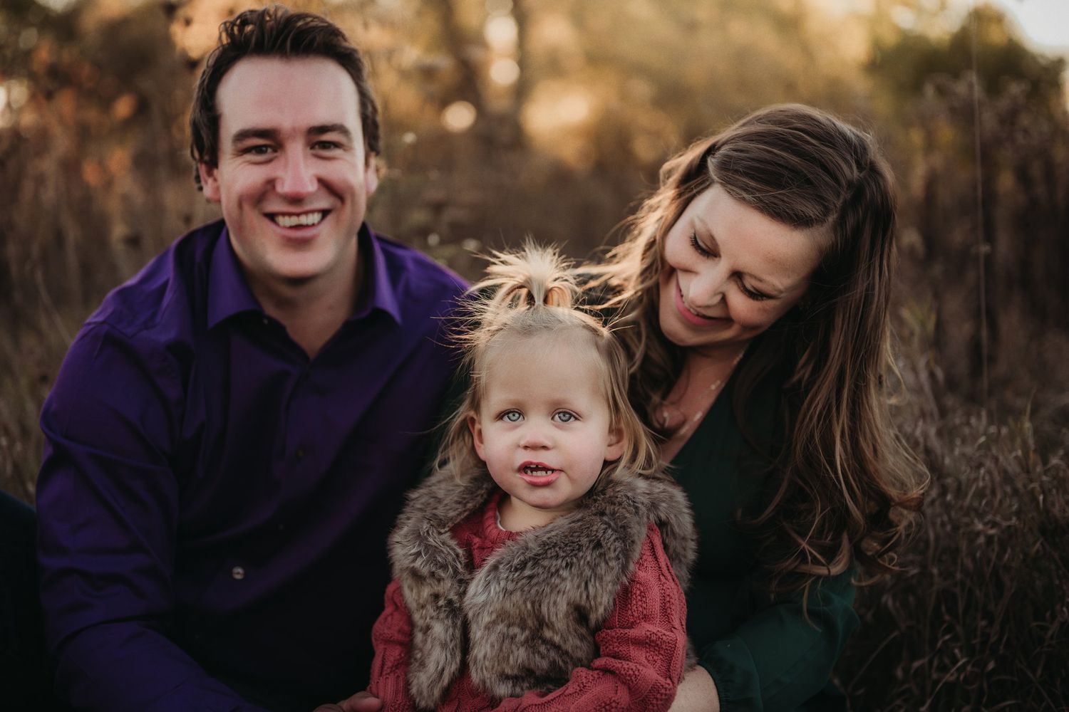 Family portrait in warm evening light with purple and green clothing against natural backdrop.