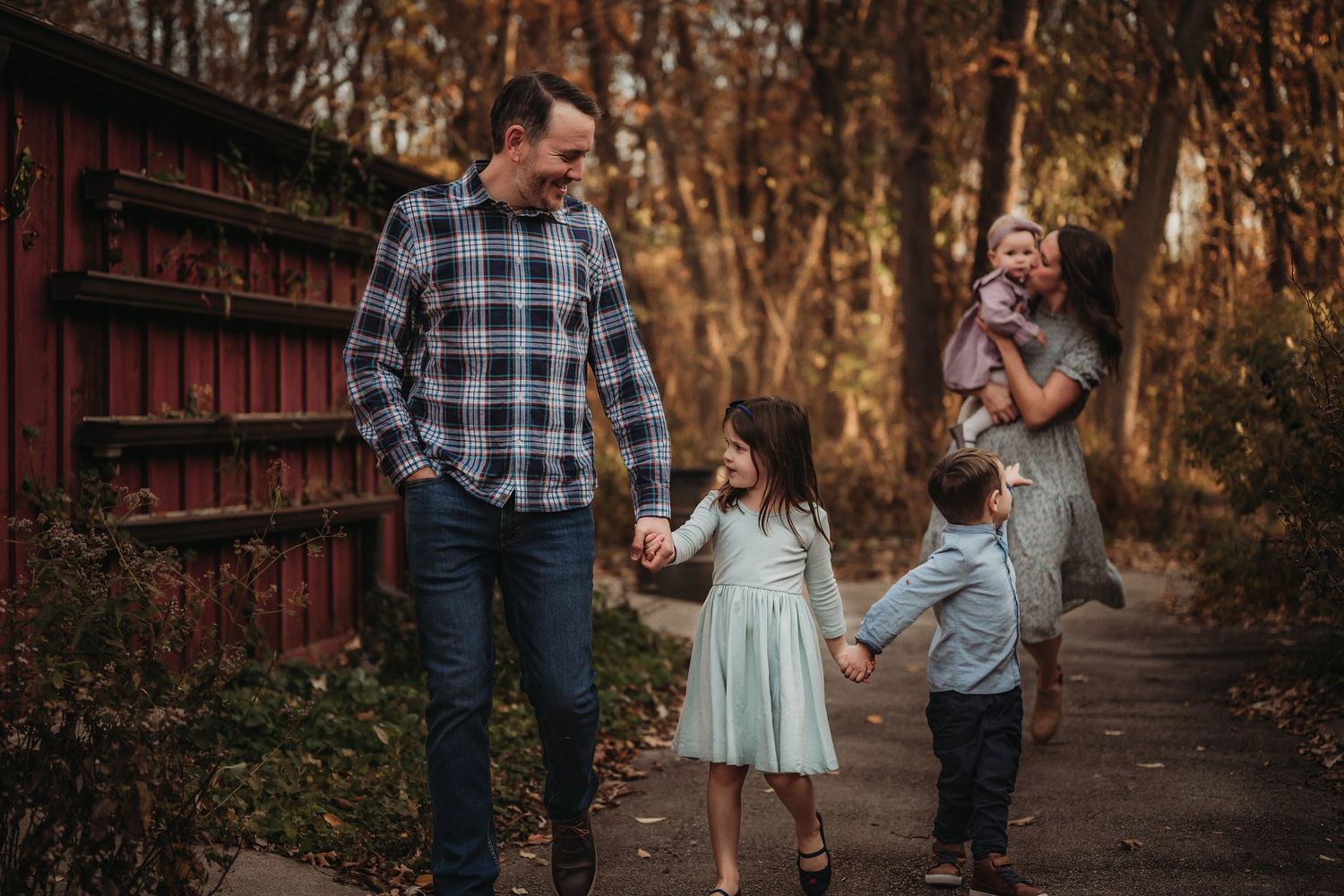 Autumn family walk along wooded path with red barn in background during golden hour.