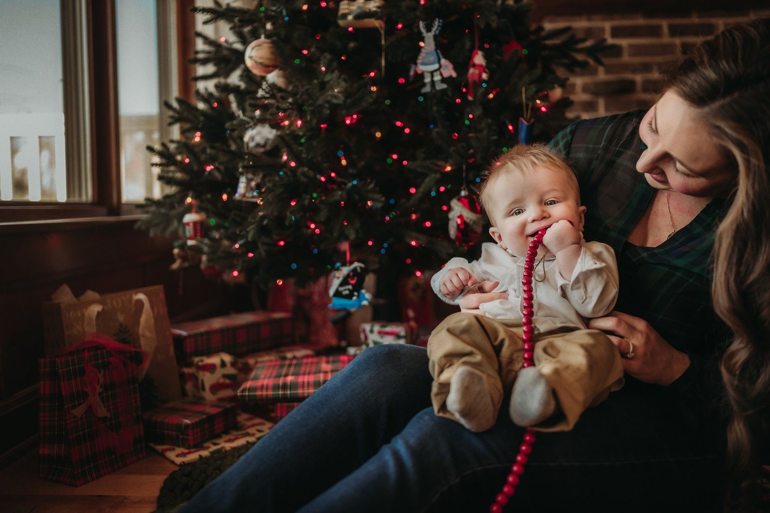 Heartwarming Christmas moment by a decorated tree with red beads and plaid blankets.