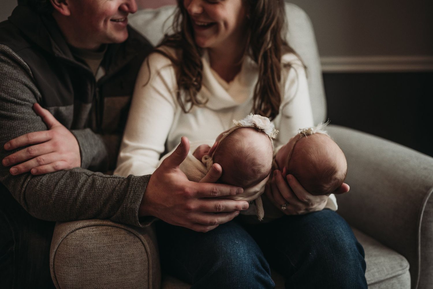 Intimate family moment with newborn twins being held on dark leather couch.