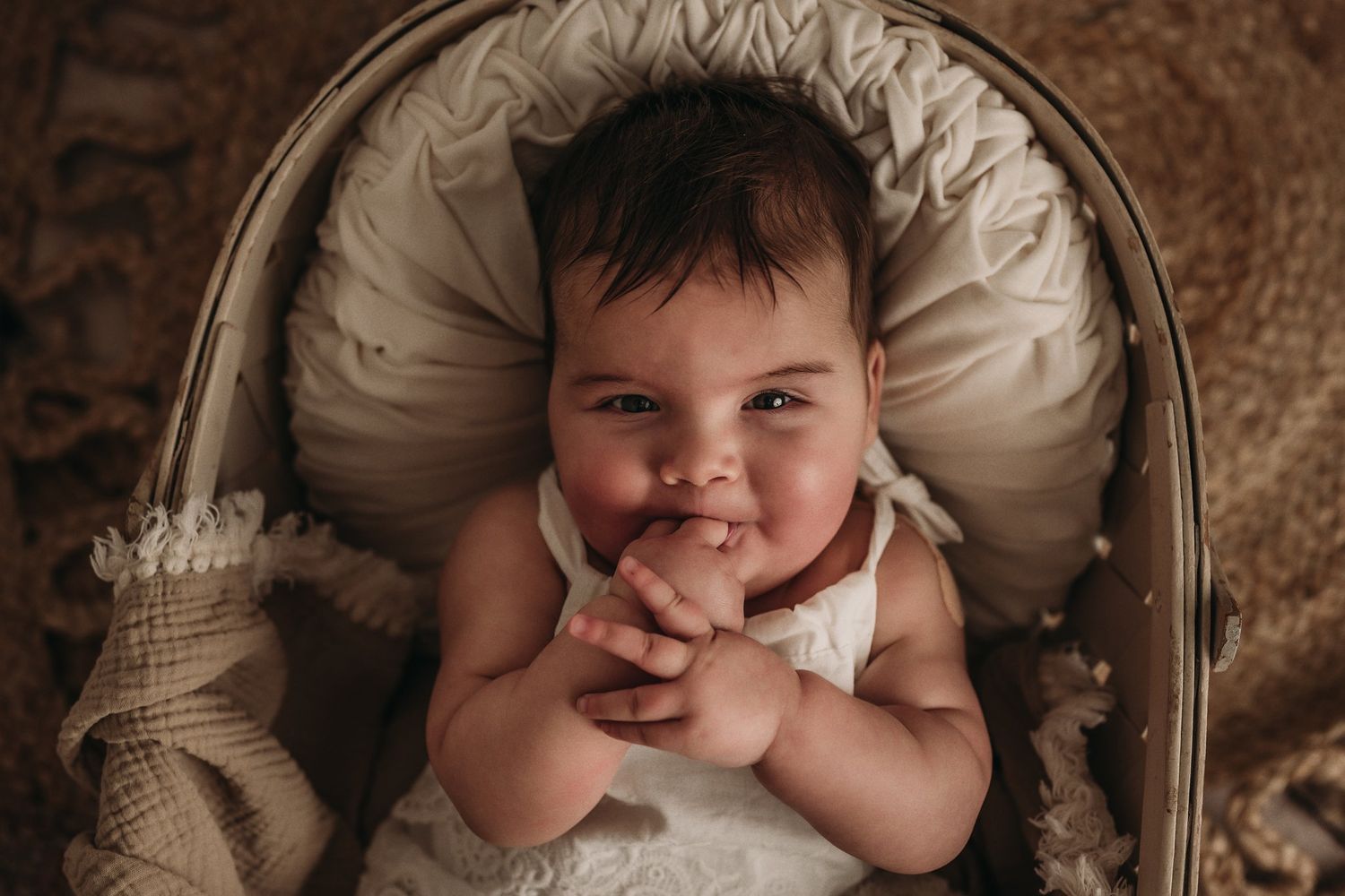 Baby in white outfit smiles while resting in vintage-style cream bassinet.