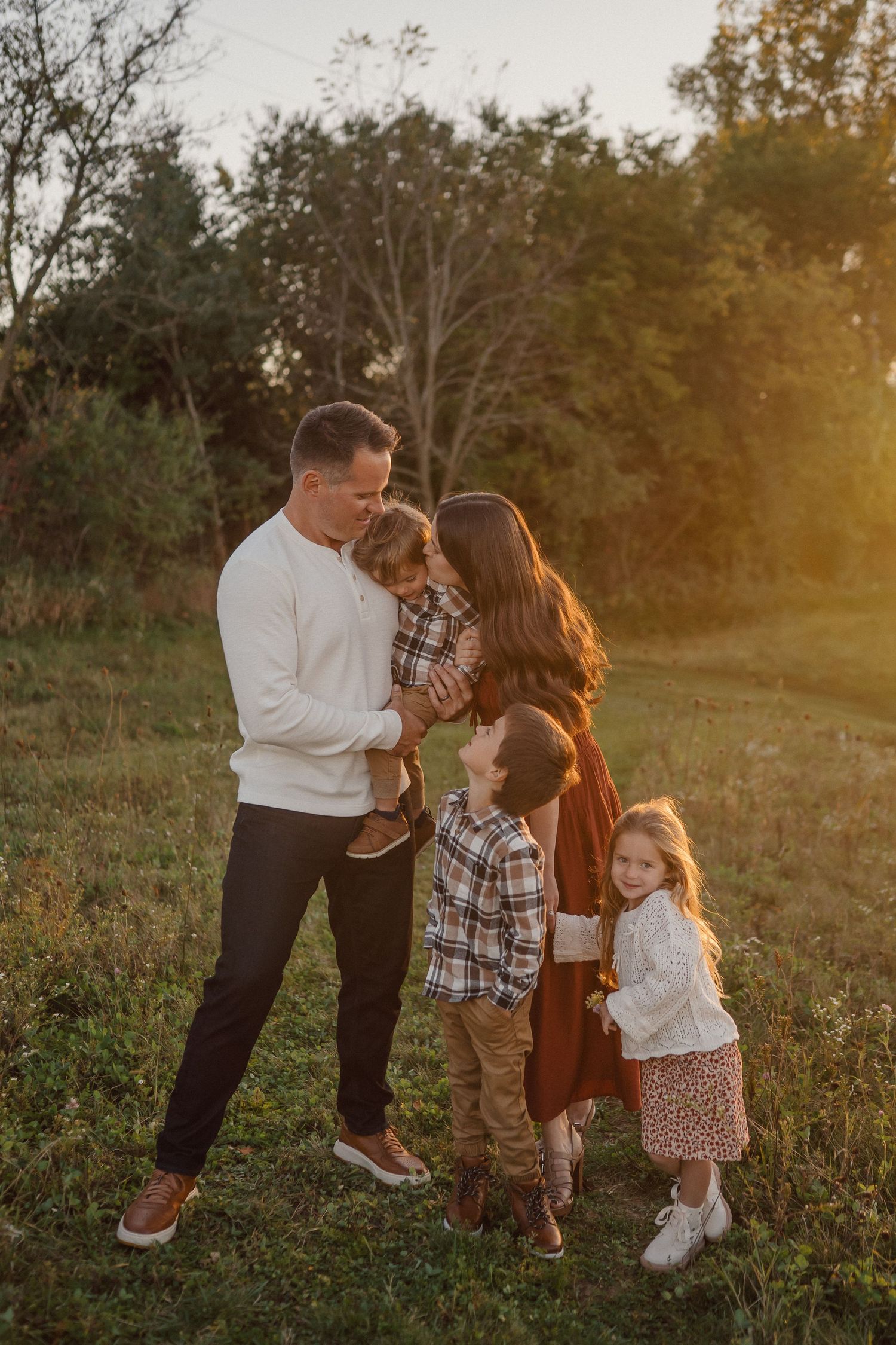 Family of five poses together during sunset photoshoot in a rustic field setting.