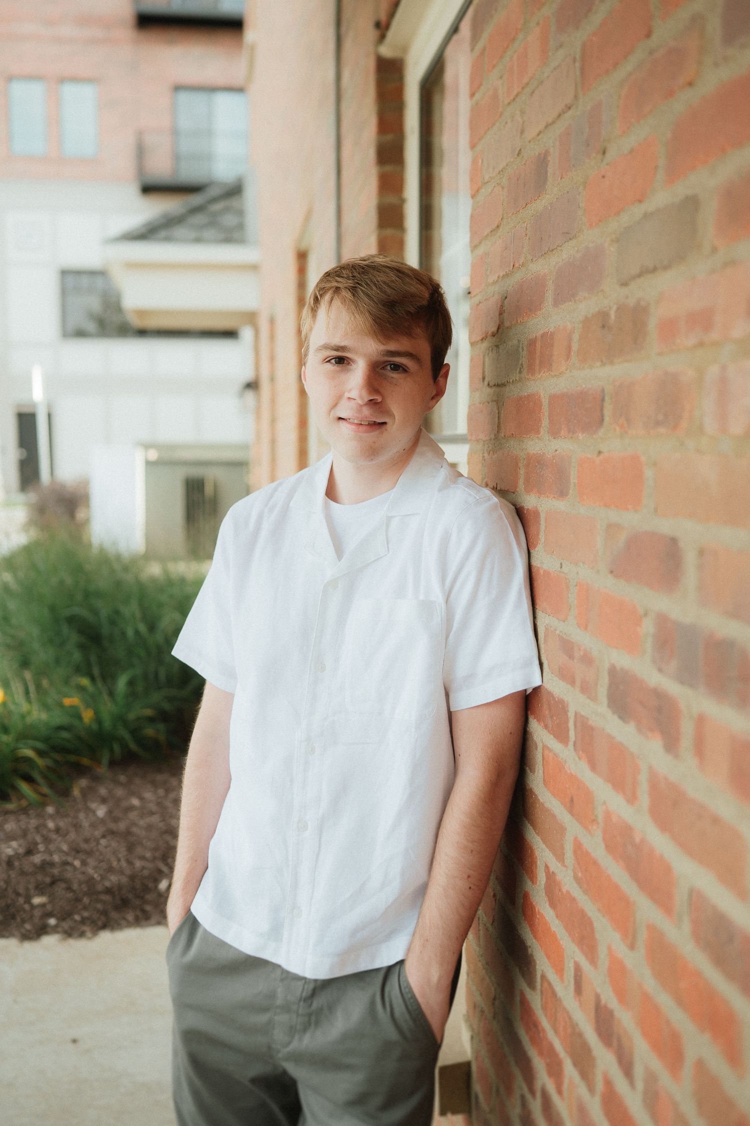 A person in a white t-shirt leans against a brick wall on a sunny day.