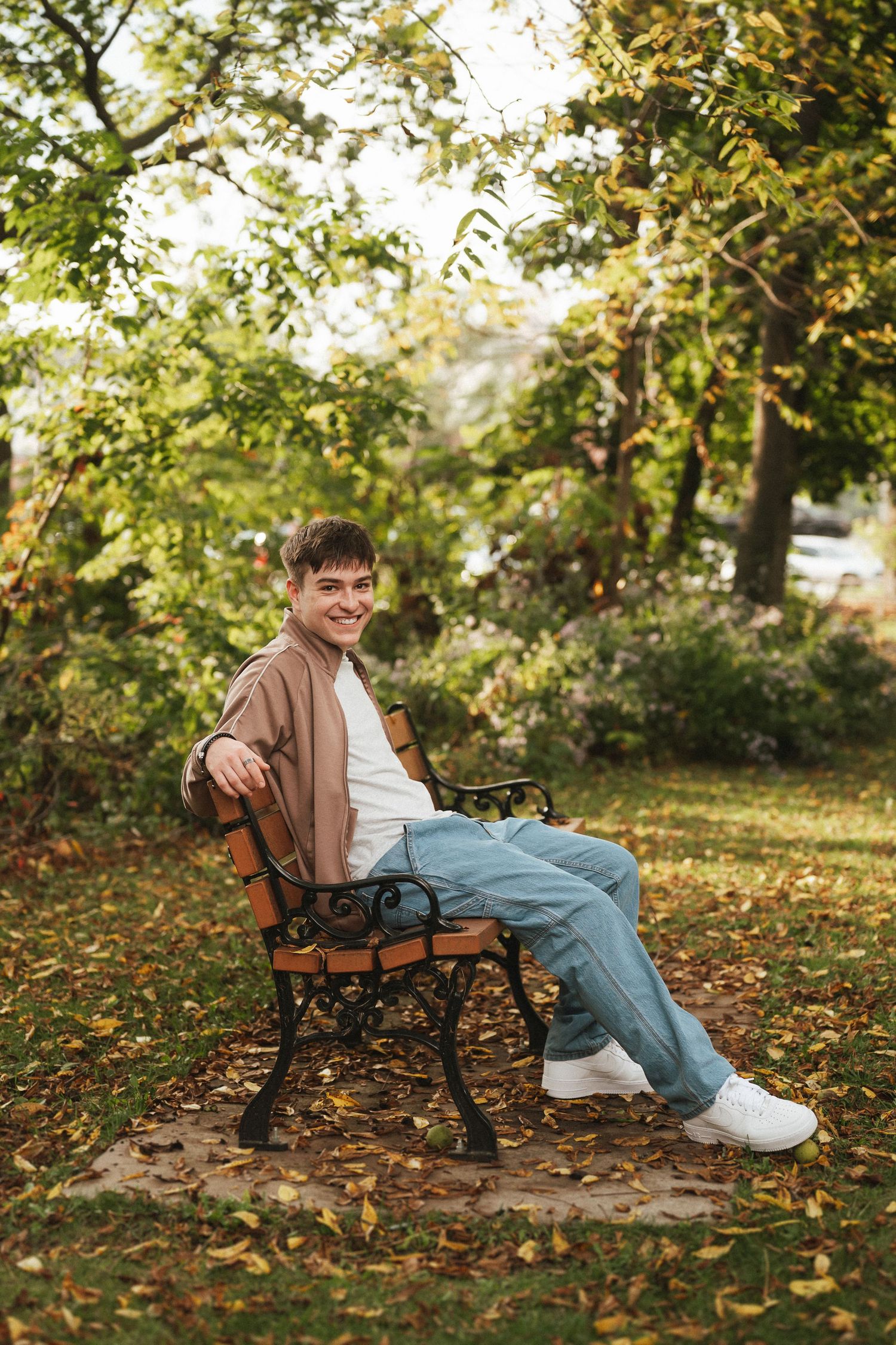 Person relaxing on a park bench surrounded by autumn leaves and golden sunlight in a peaceful outdoor setting.