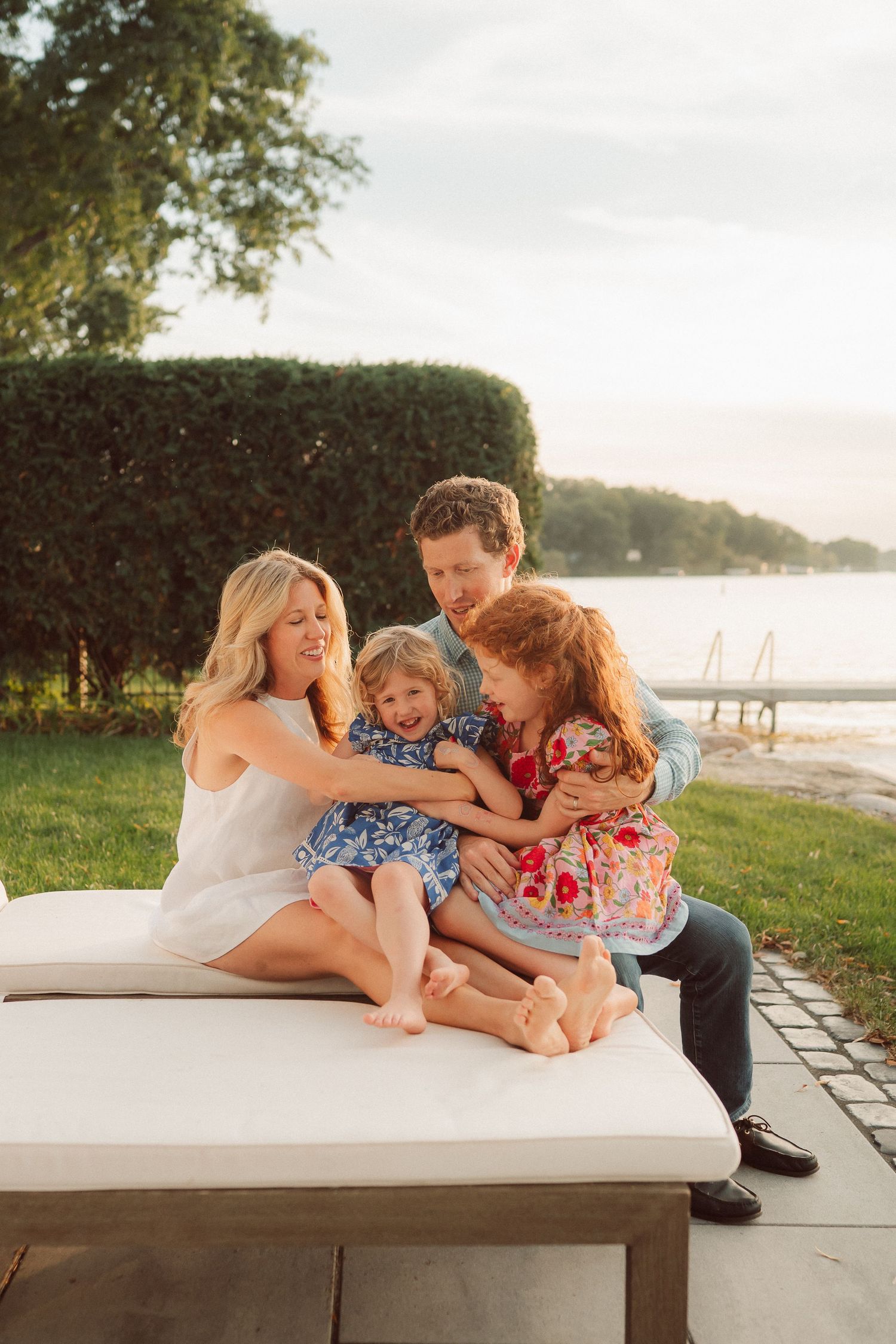 Family relaxing together on a white bench near a waterfront during sunset.