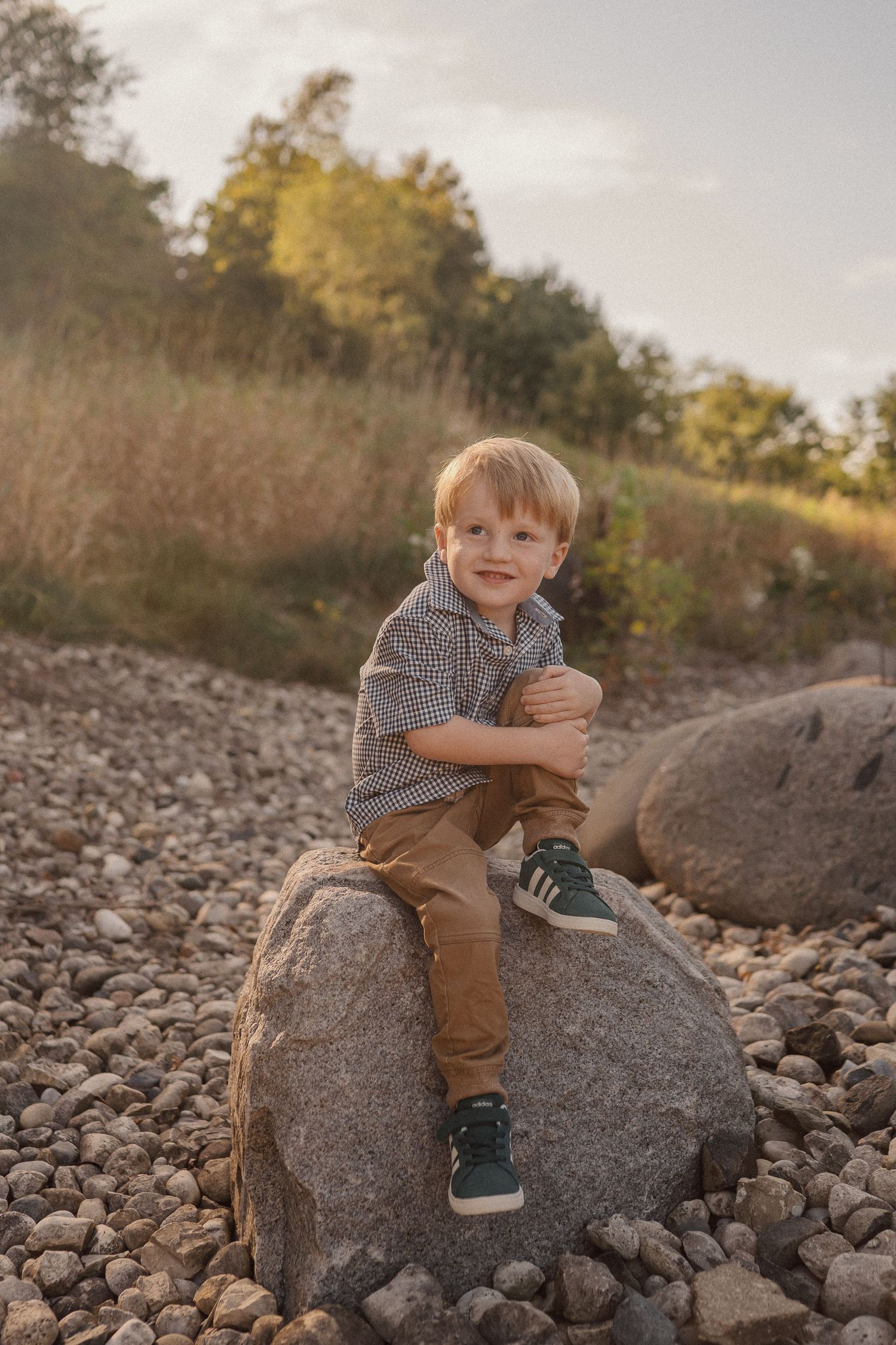 A young child sits playfully on a large rock among a rocky terrain.