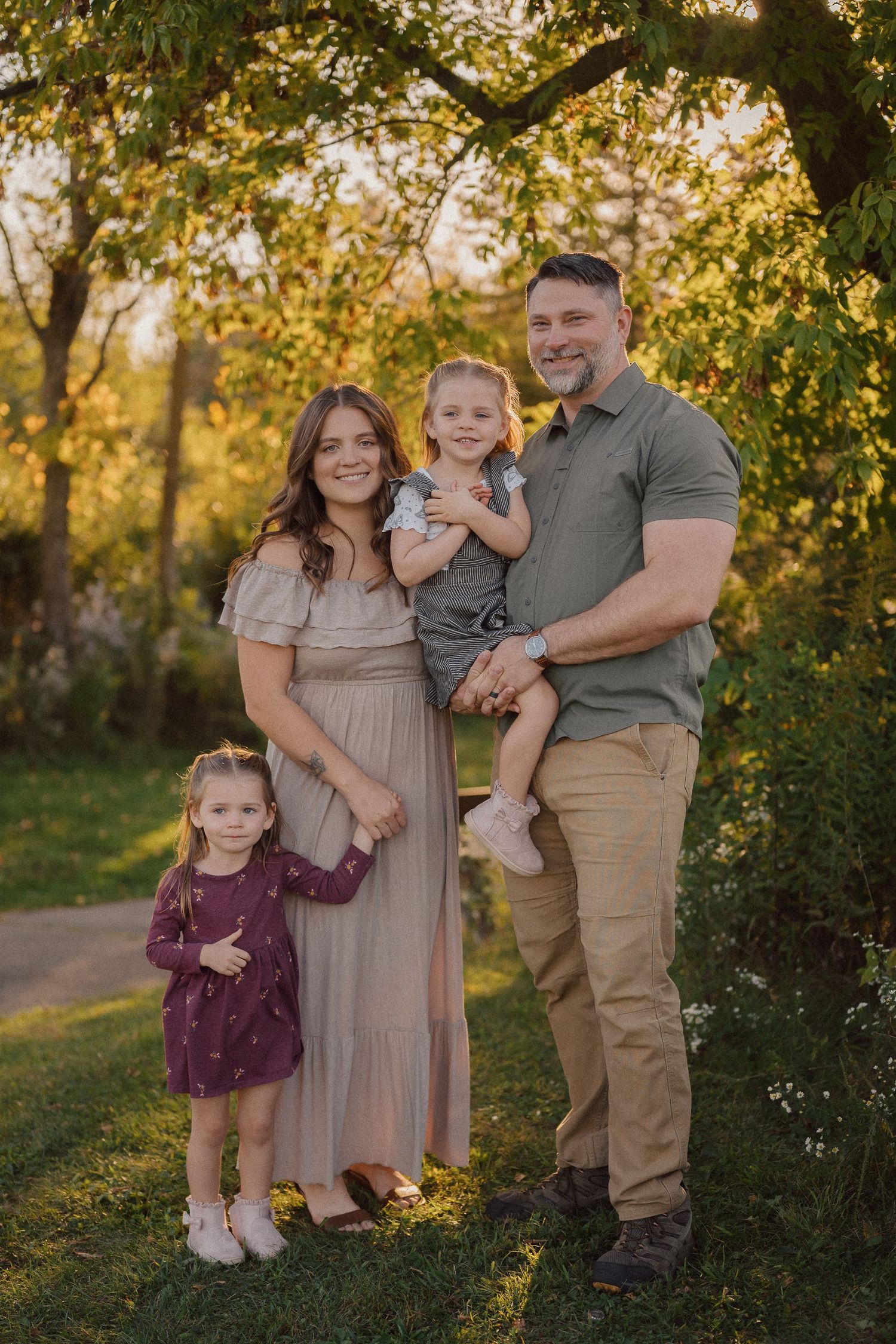 A family poses together outdoors during golden hour with autumn trees in the background.