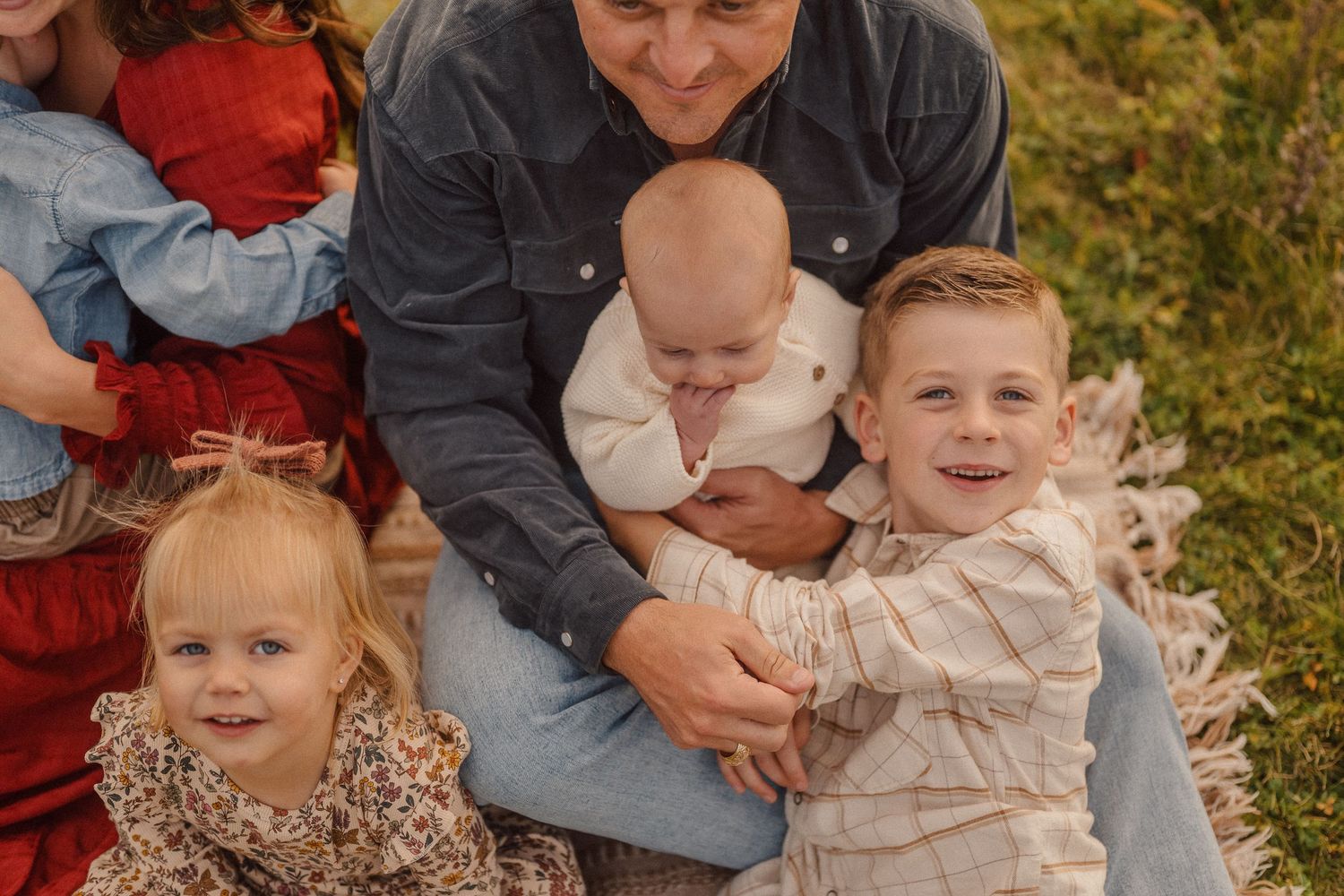 Family portrait session outdoors with everyone sitting close together in autumn field.