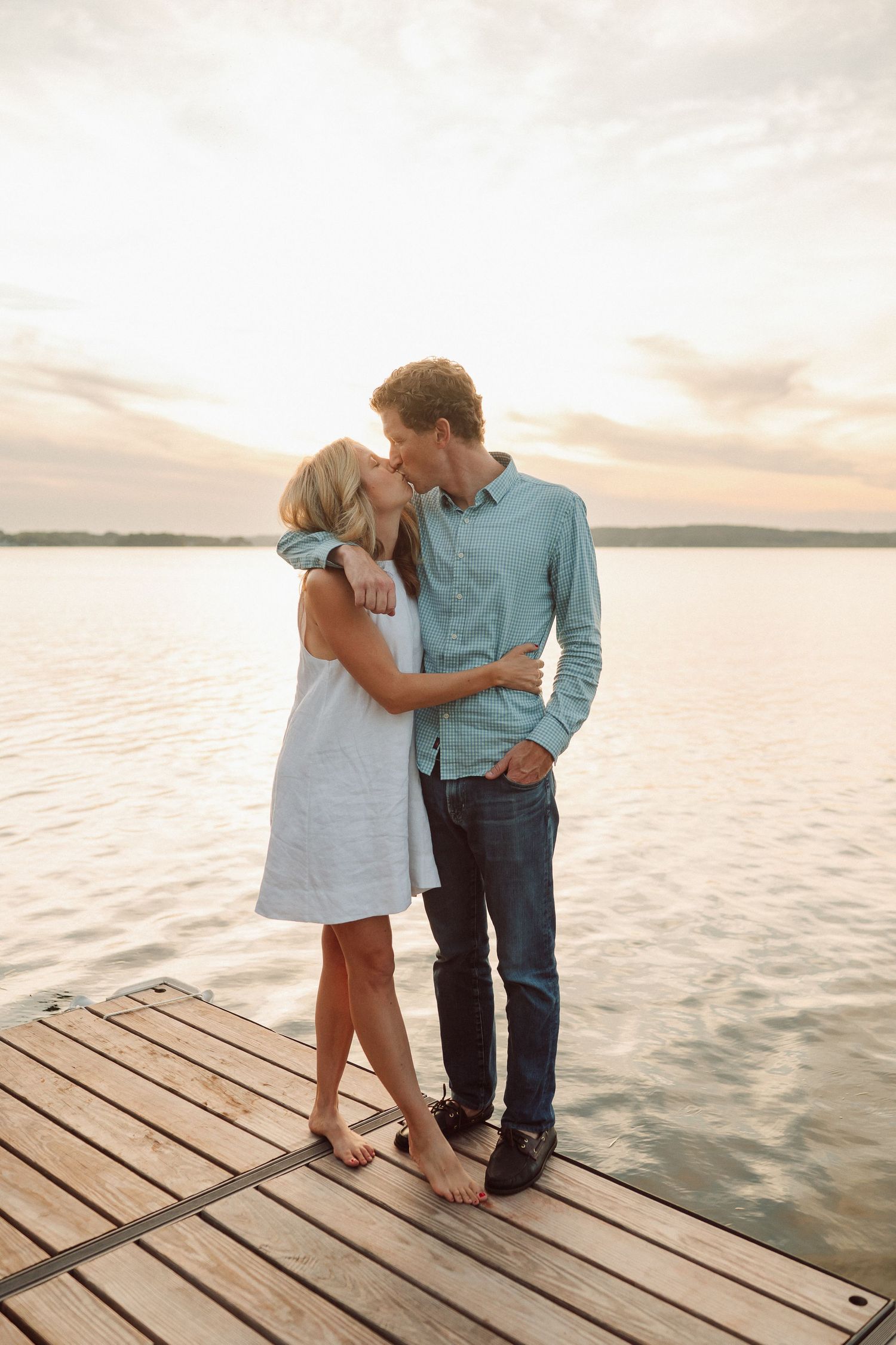 Romantic couple shares intimate moments on a wooden dock by the water during sunset.