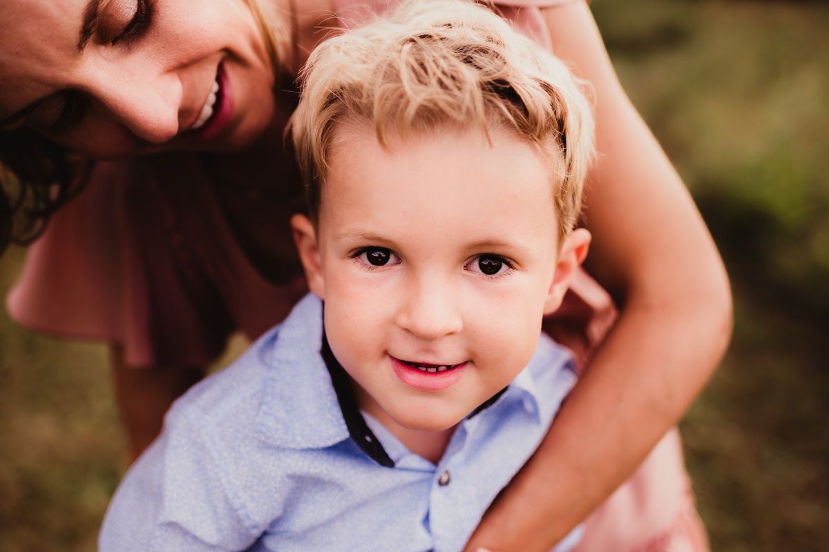 A close-up outdoor portrait of a young child in a light blue shirt against tall grass.
