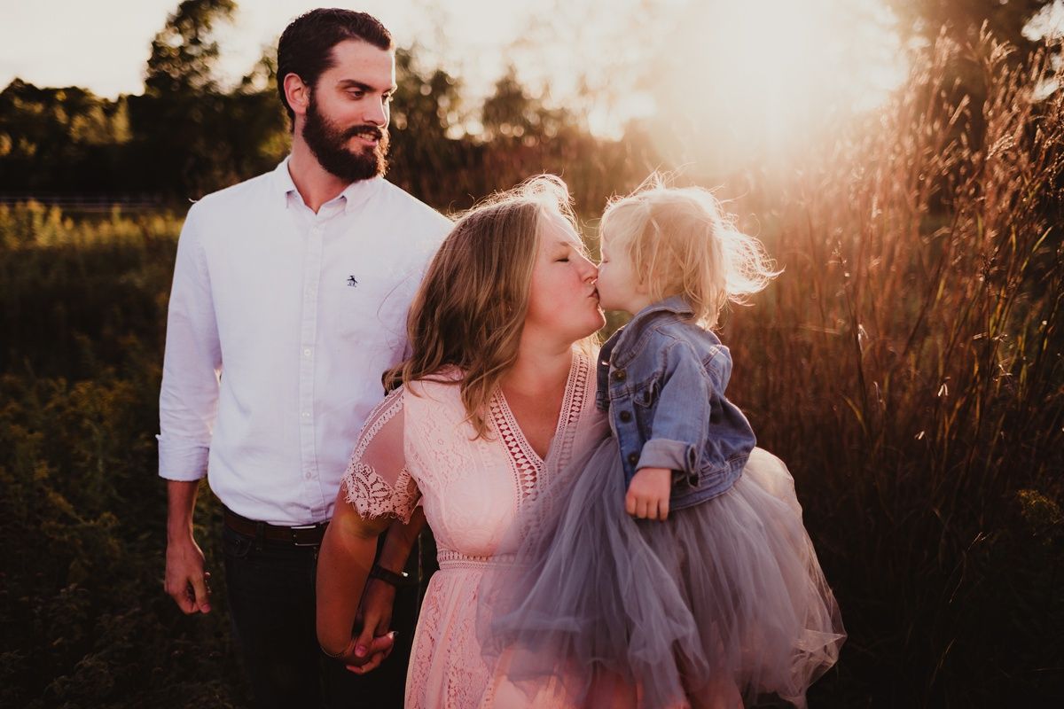 Golden hour family portrait showing tender moment amidst tall grass and warm sunlight.