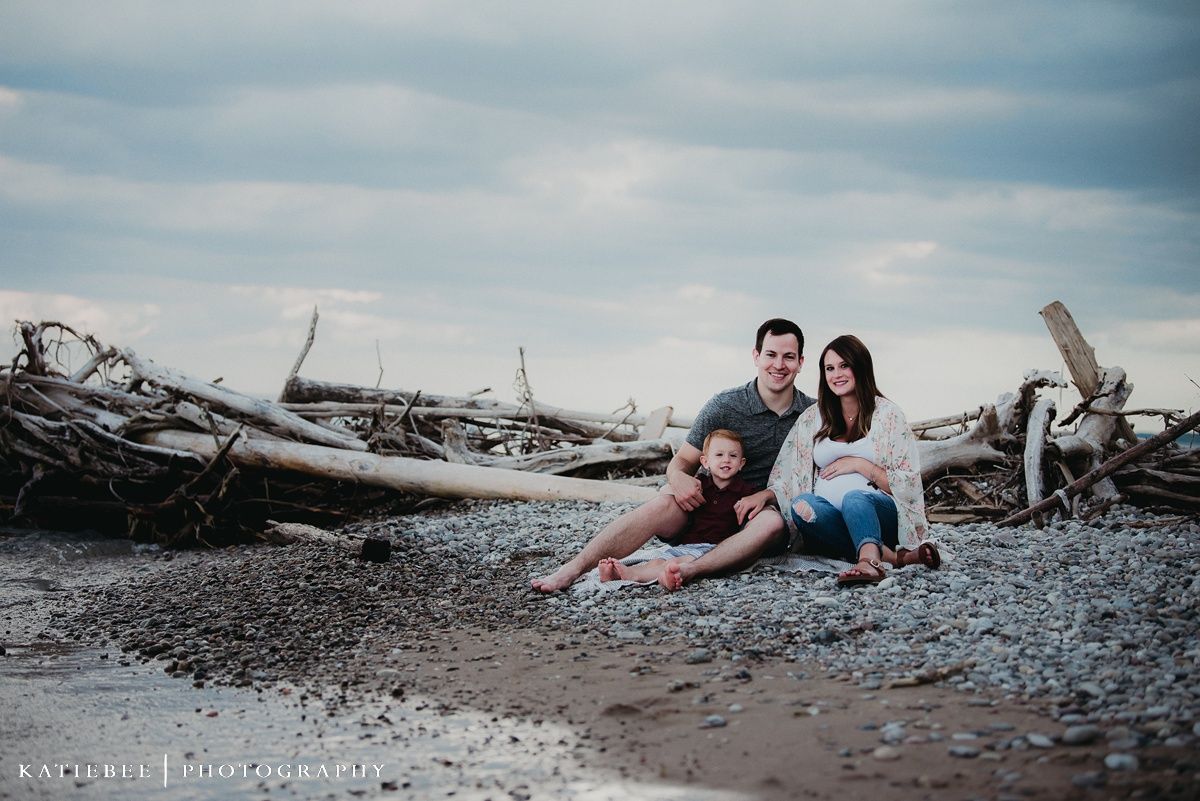 A relaxed family photo session on a rocky beach with driftwood and moody skies.