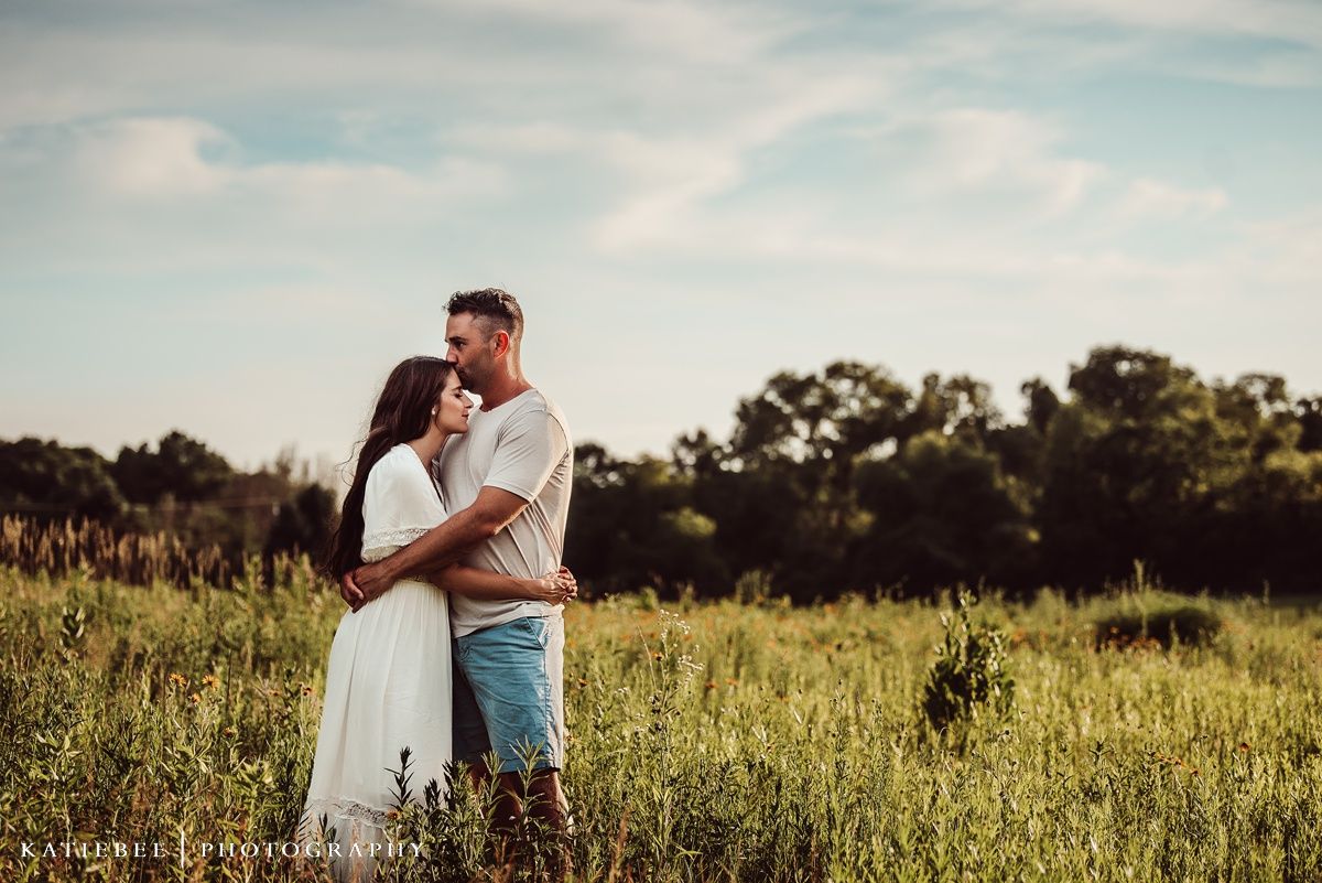 Romantic couple embracing in tall grass field during sunset photoshoot.