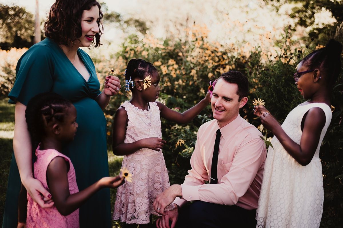 A group gathers outdoors for a casual conversation in a sunlit garden setting.