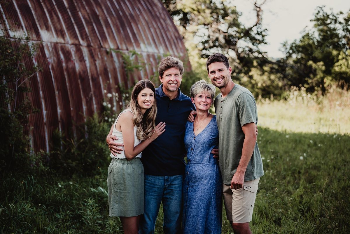 Family portrait taken outdoors with rustic barn background during golden hour.