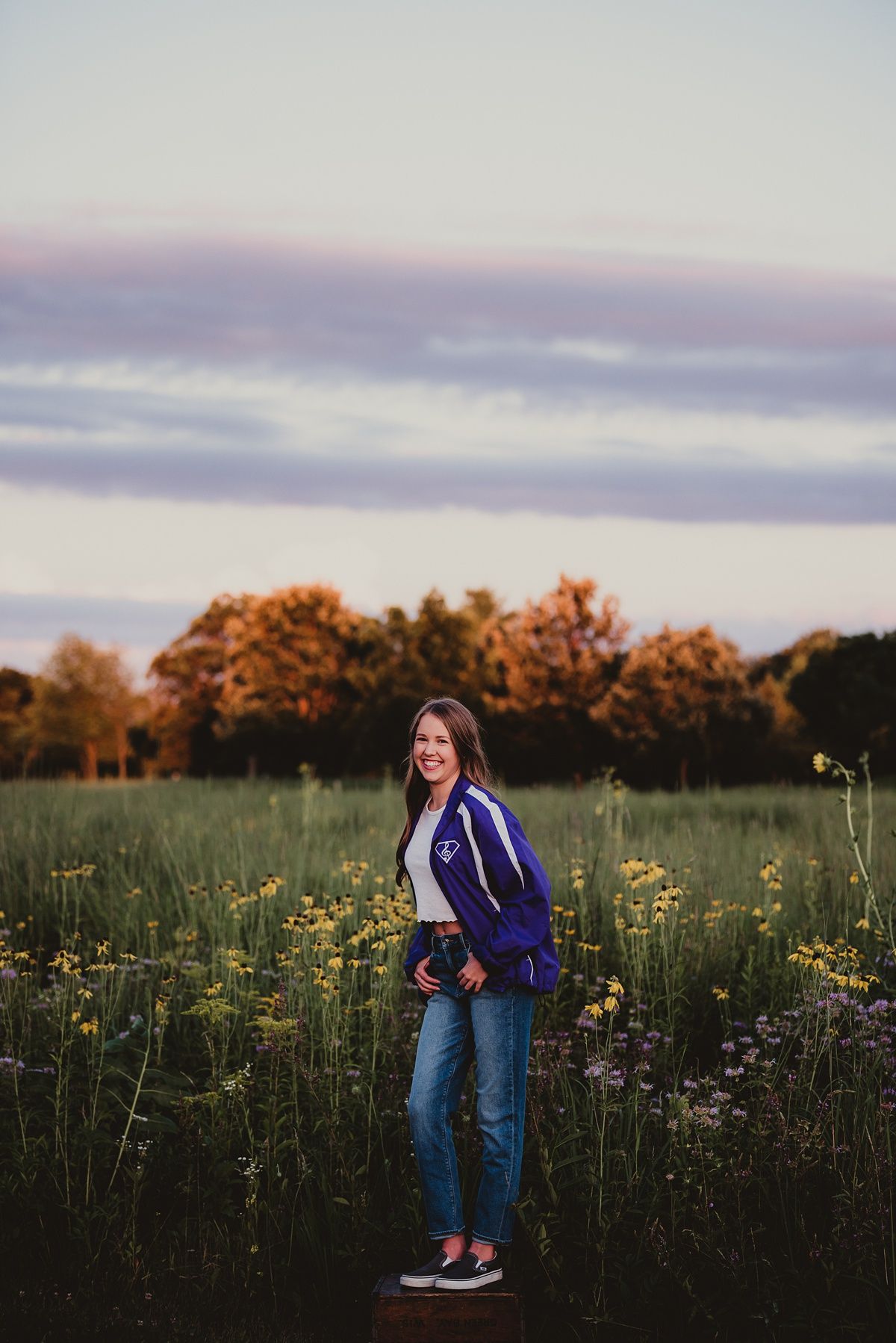 A casual portrait in a purple jacket among yellow wildflowers at sunset.