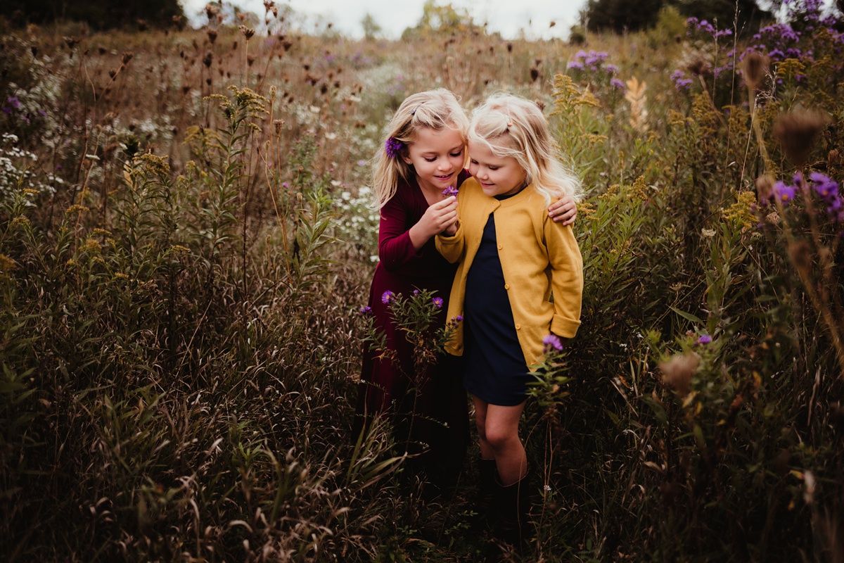 Two children play together in a wild autumn meadow with tall grass and flowers.