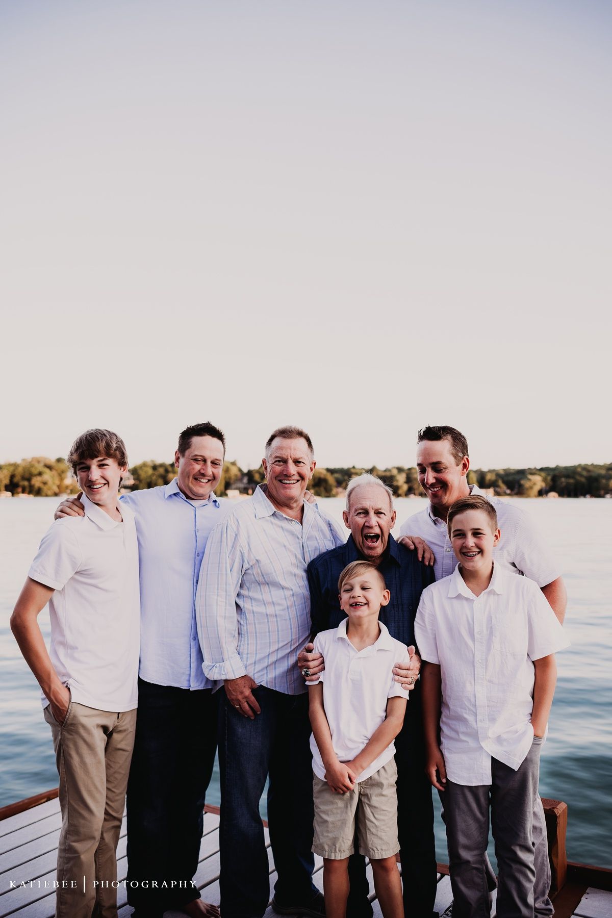 Male family members of different generations pose together on dock by lake at sunset.