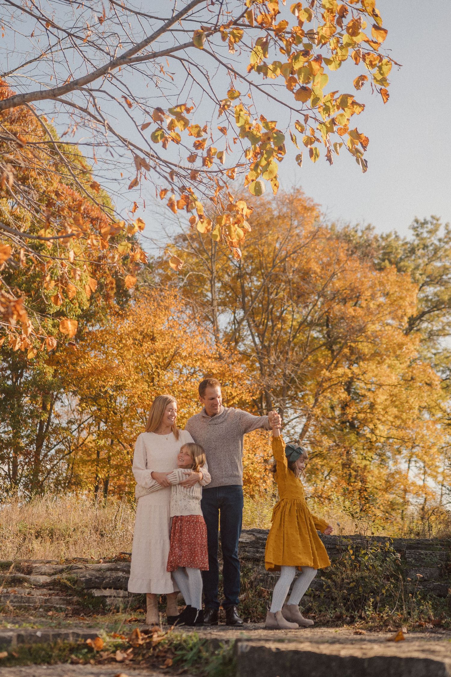 Family portrait session in a natural setting with autumn trees displaying golden leaves.