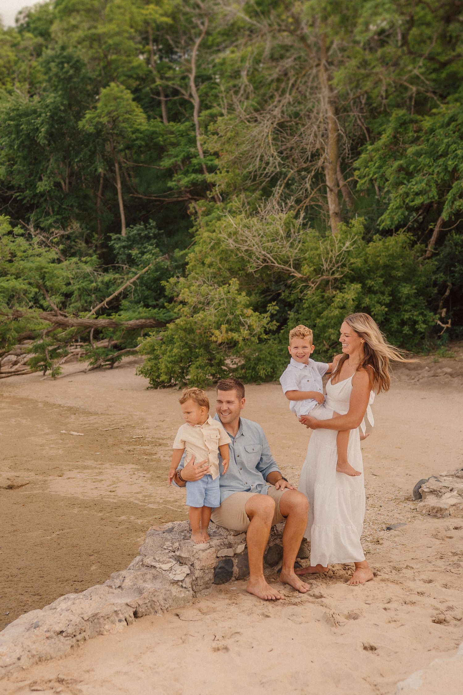 Family portrait on a sandy beach with green foliage backdrop during golden hour.