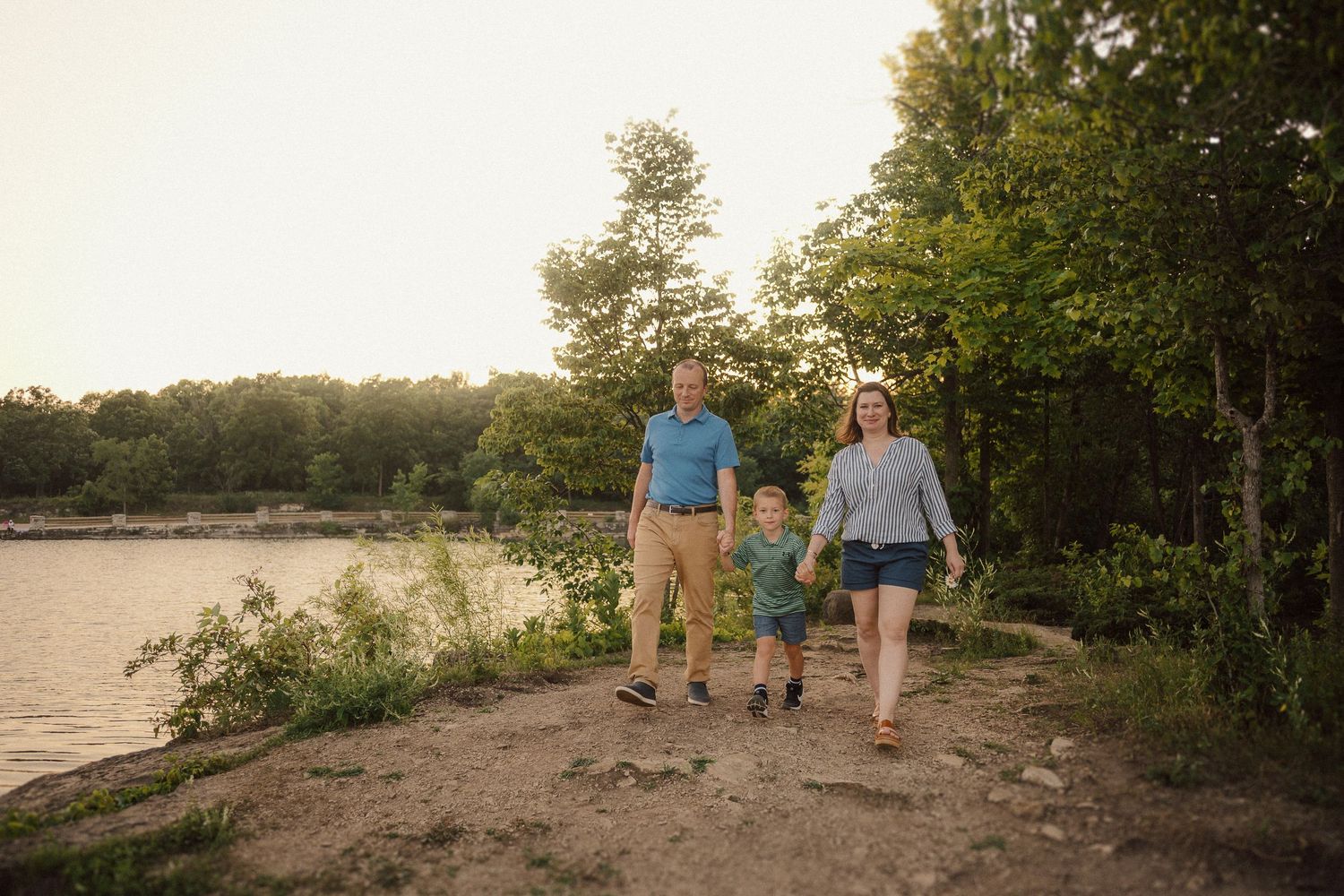 Family enjoys an evening walk along a scenic riverbank during golden hour.