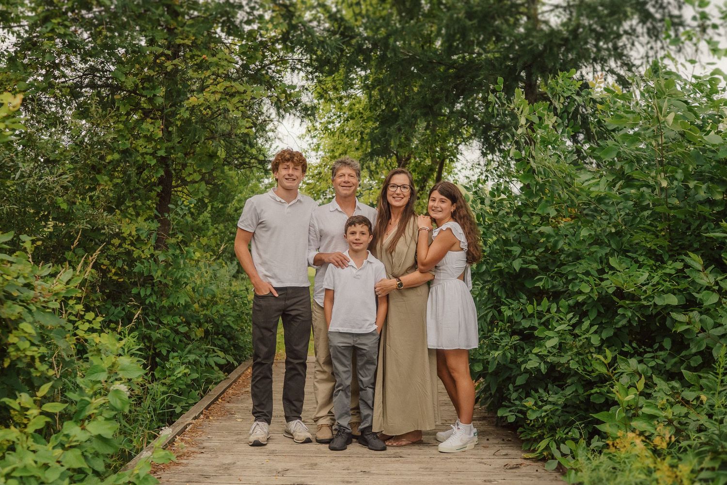 A family group poses together on a wooden walkway surrounded by verdant summer foliage.