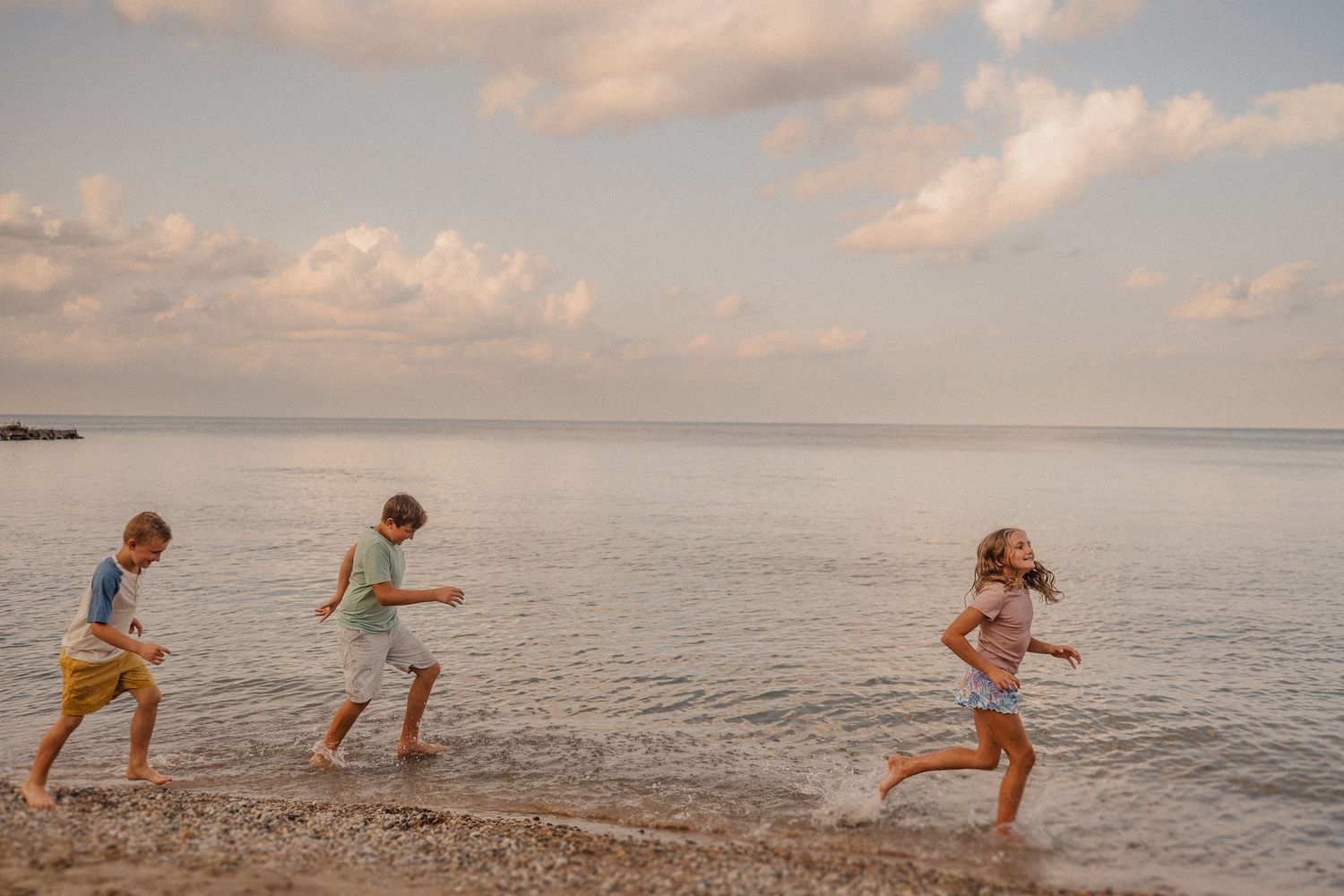 Three people running along the shoreline at sunset with calm ocean waters in the background.
