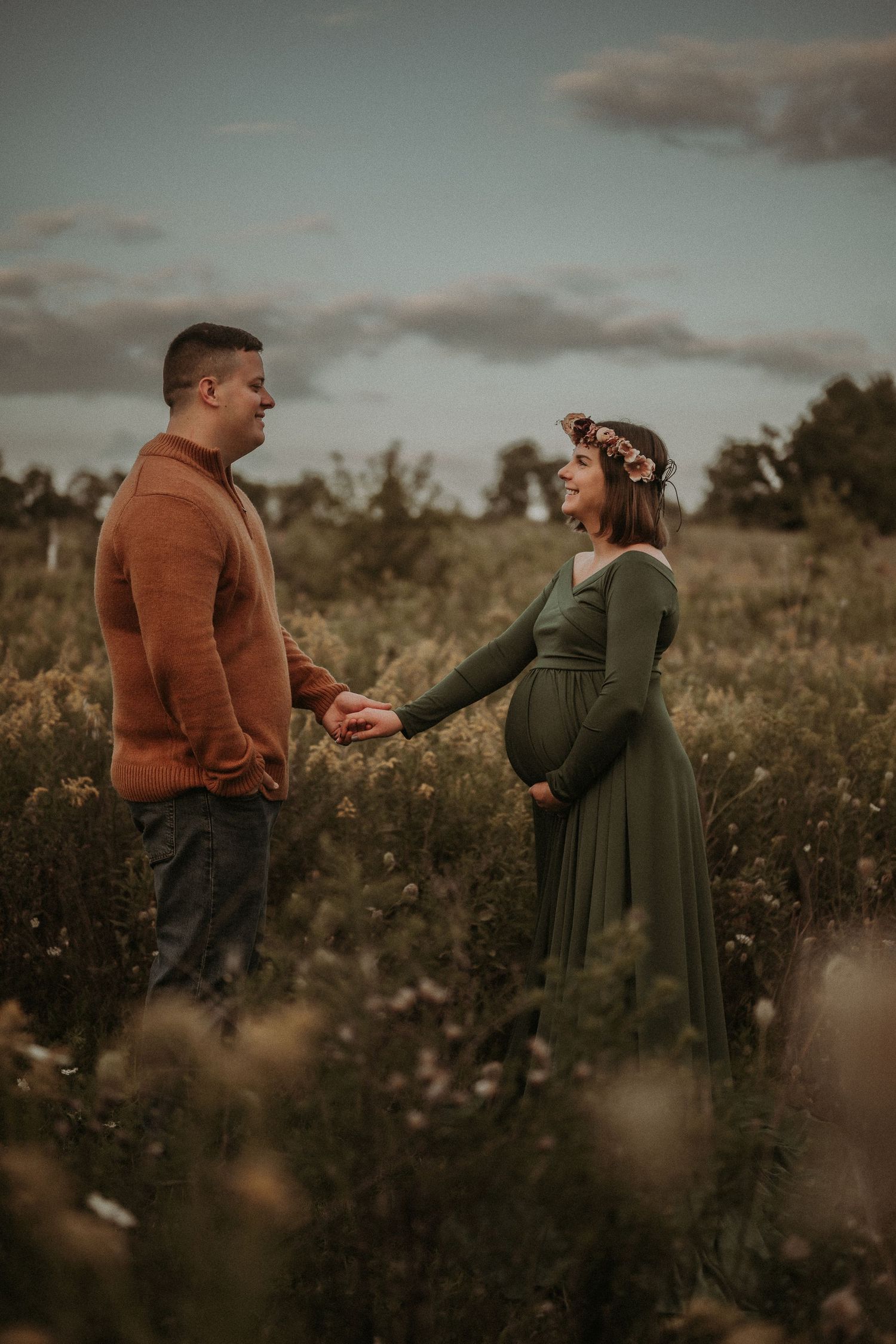 A couple shares an intimate moment in a field, with her in green and him in rust-colored sweater.