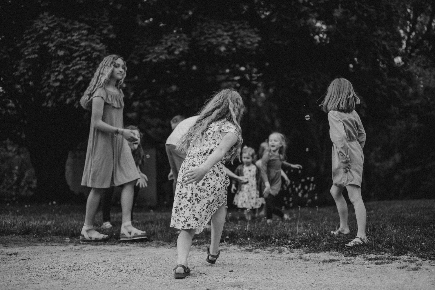 Children play and run on a path outdoors in black and white photography.