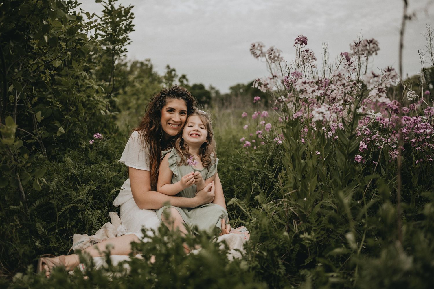 A peaceful family portrait taken in a lush garden with pink flowers blooming in the background.