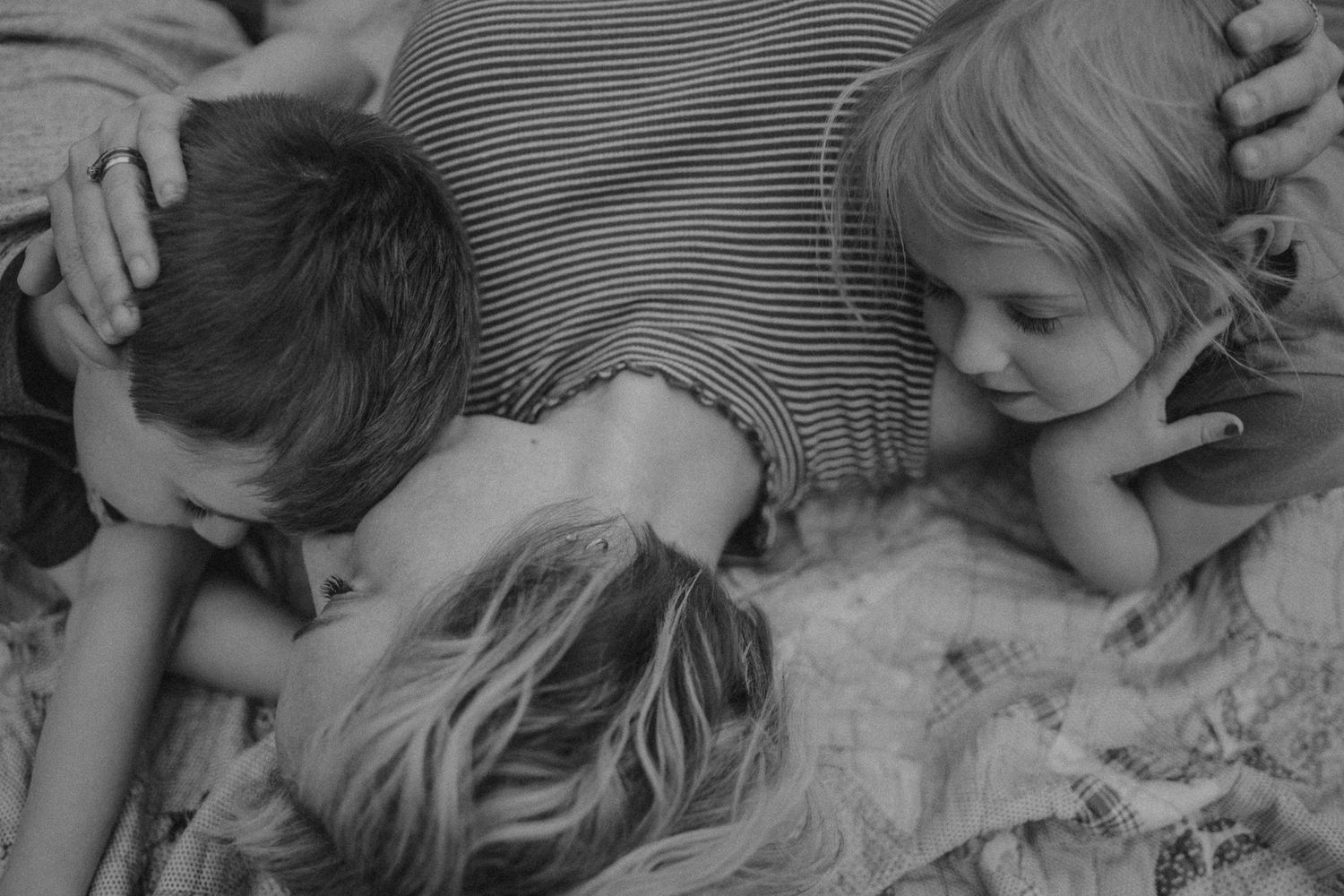 Black and white image of family members cuddling together on a soft surface.