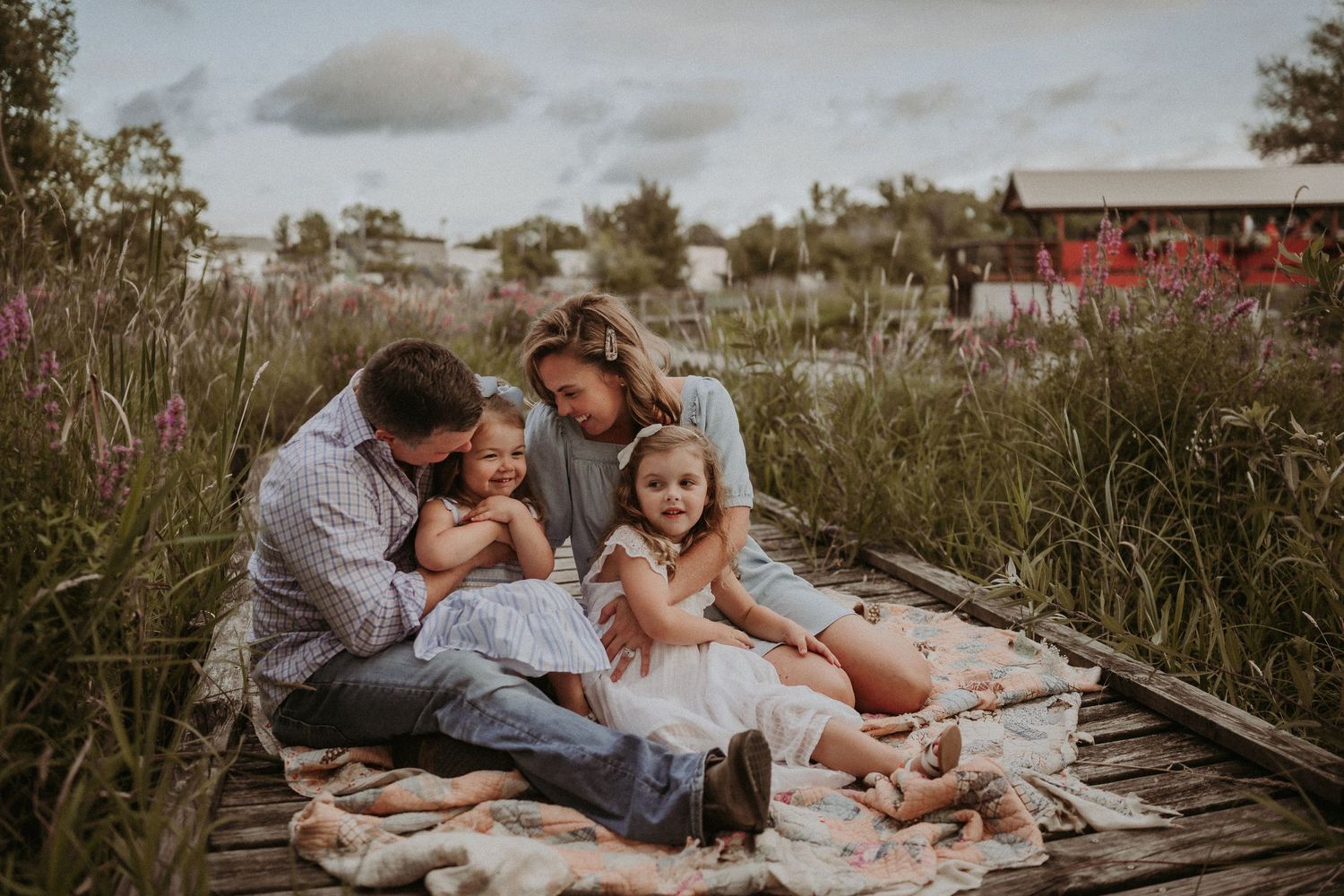 Candid family moment captured on blanket during golden hour with rustic backdrop.