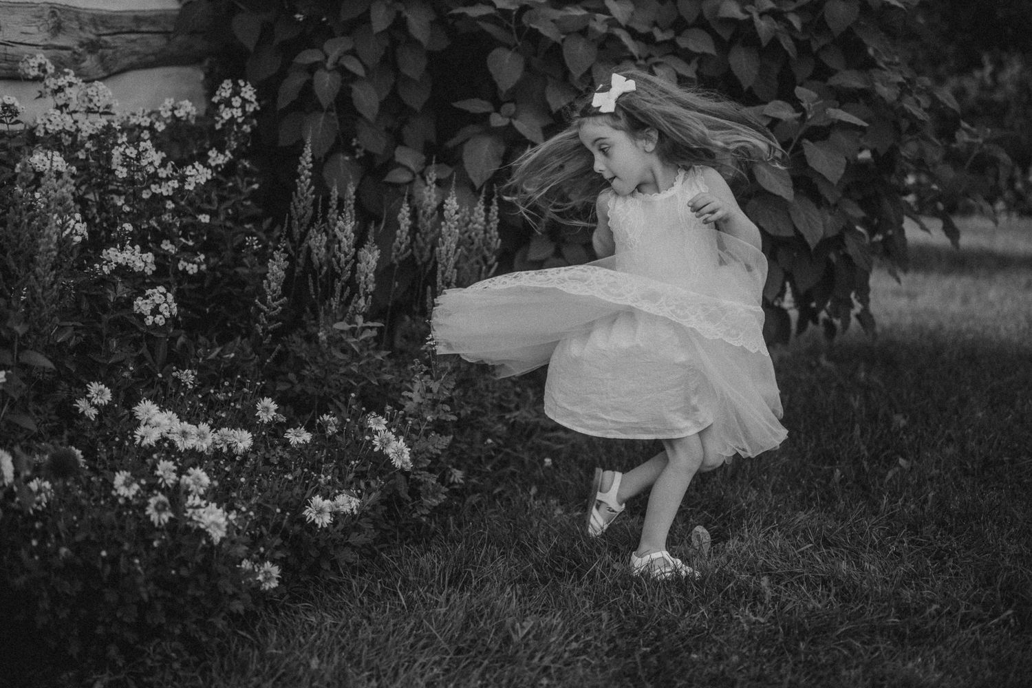 Black and white photo of flowing white dress twirling in garden setting.
