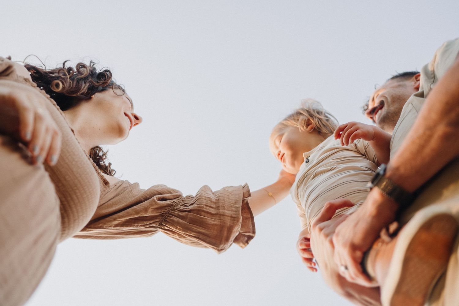 Low angle view of three people leaning together against a bright sky background.
