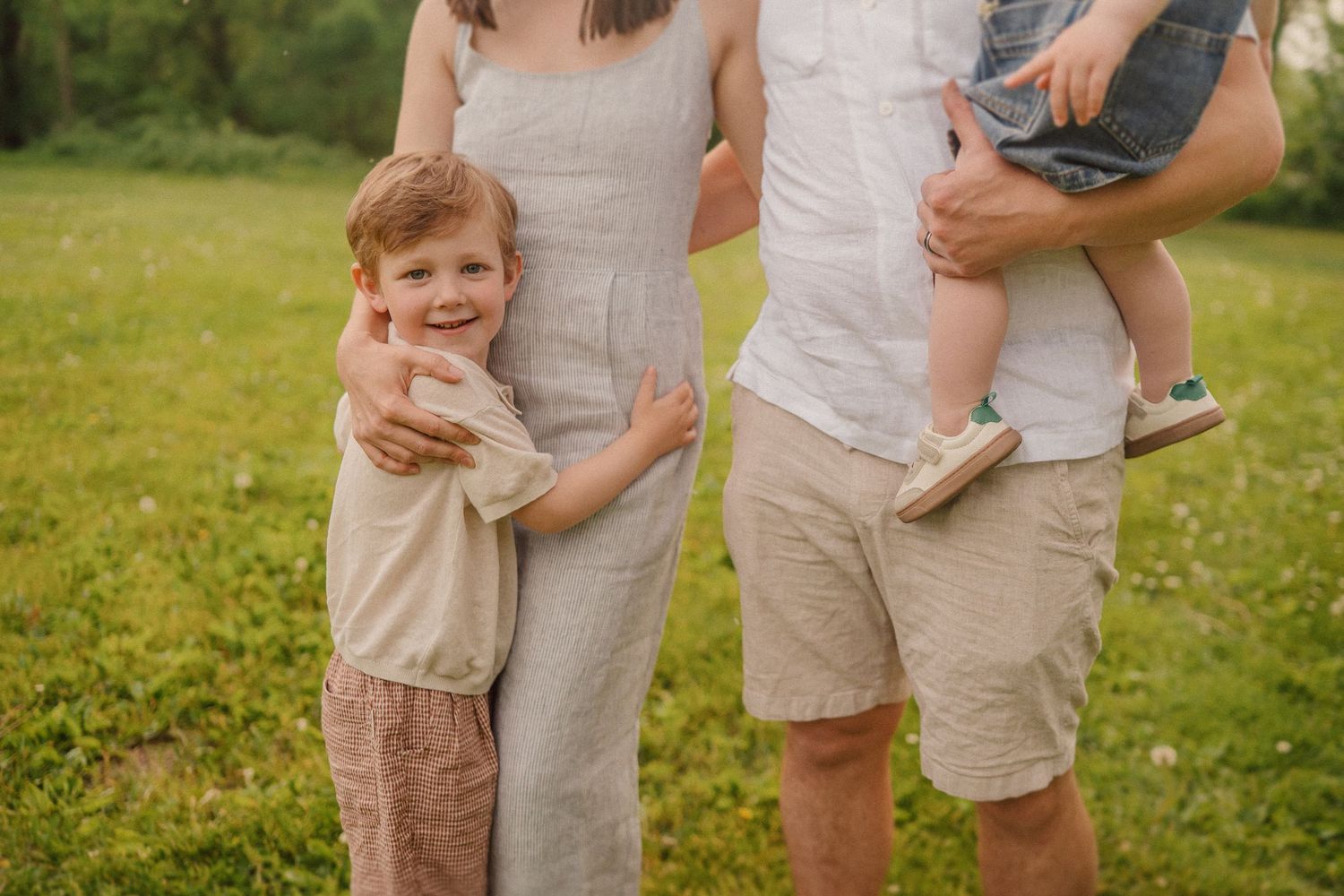 A family stands together on a grassy field wearing matching light colored casual summer outfits.