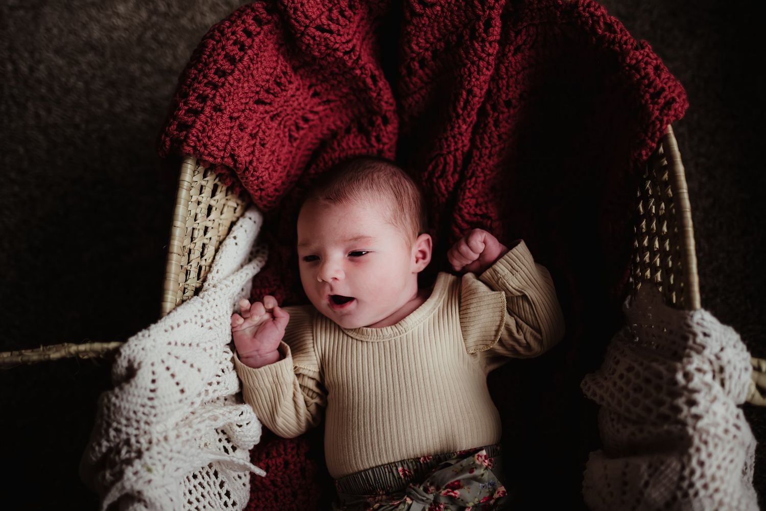 Baby relaxing on blankets in natural lighting with burgundy and cream knitted textures.