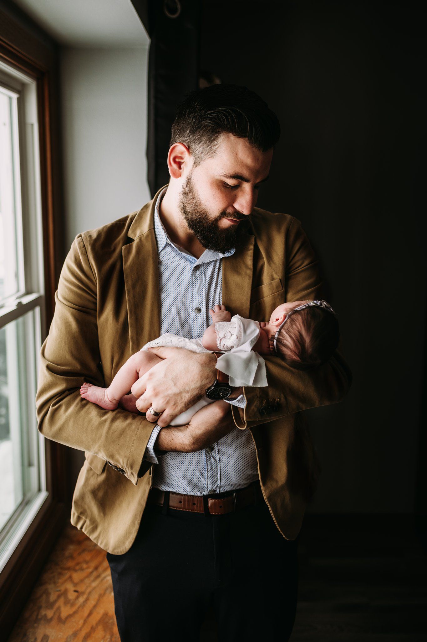 A candid moment by a window showing someone in business casual attire holding a tiny infant.