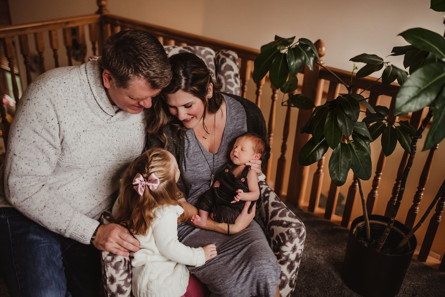 An intimate family portrait shows tender interactions while seated on a patterned armchair.