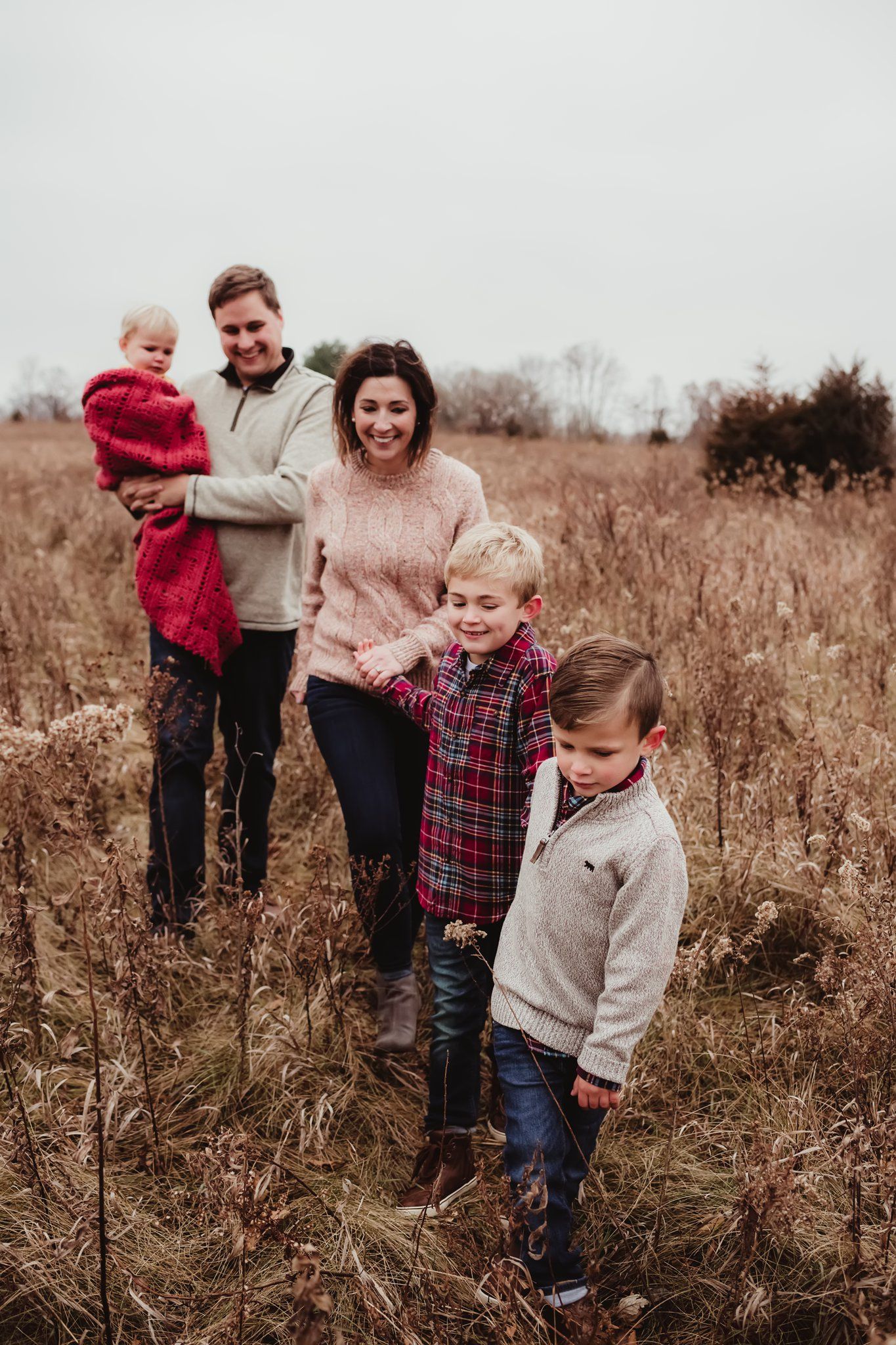 A family of five stands together in a tall grass field during autumn.