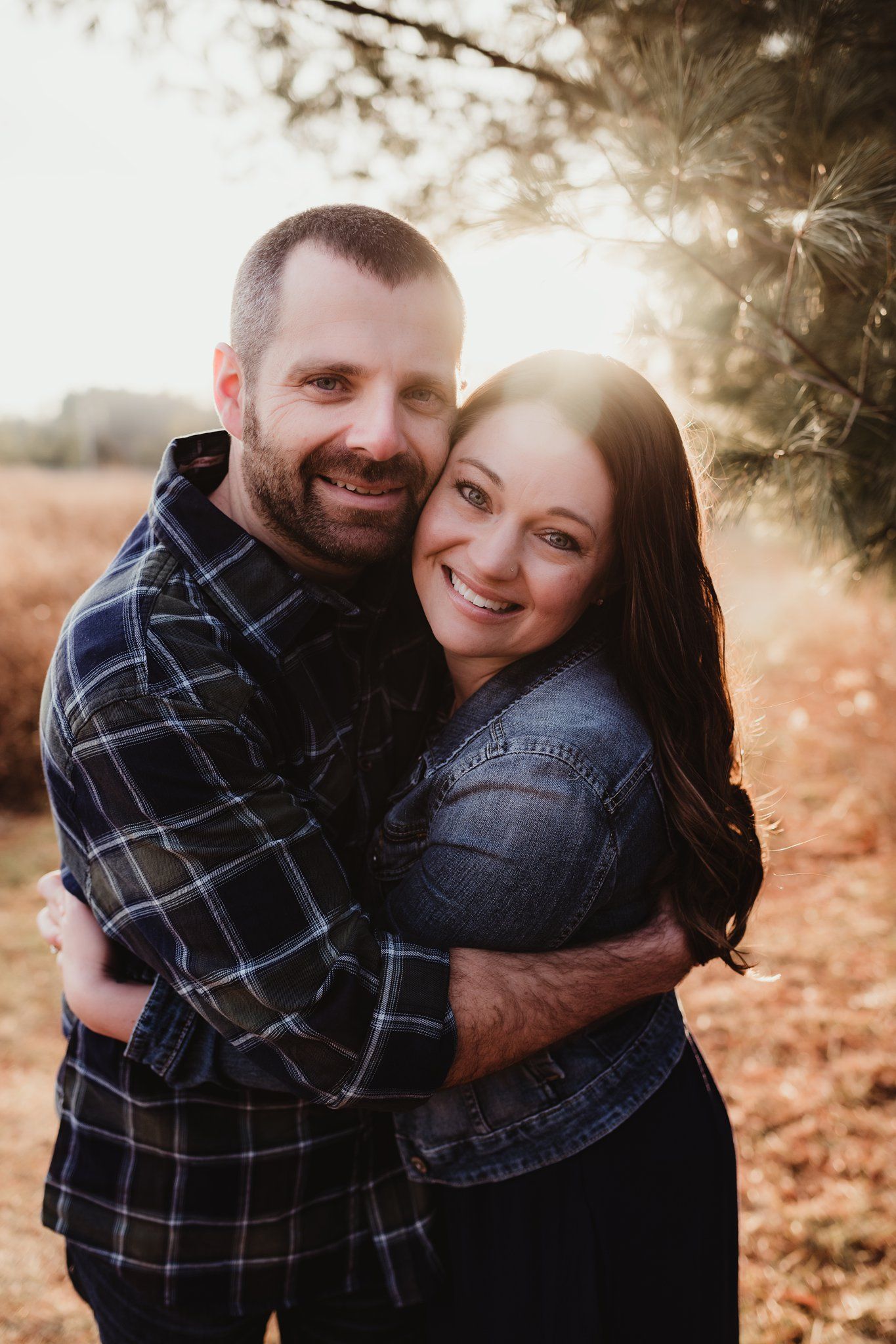 Romantic couple embracing outdoors at golden hour wearing casual plaid and denim.