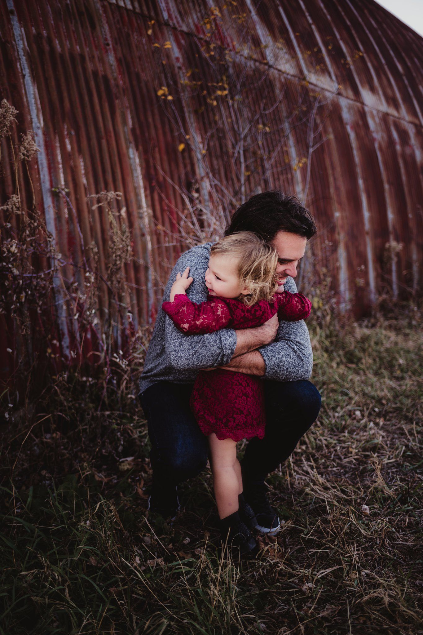 A sweet embrace captured against a rustic red wall in outdoor autumn setting.